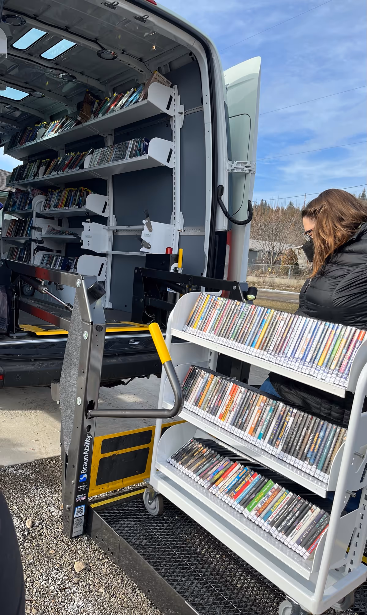 Open van rear showing book shelves and a person loading a wheeled cart.