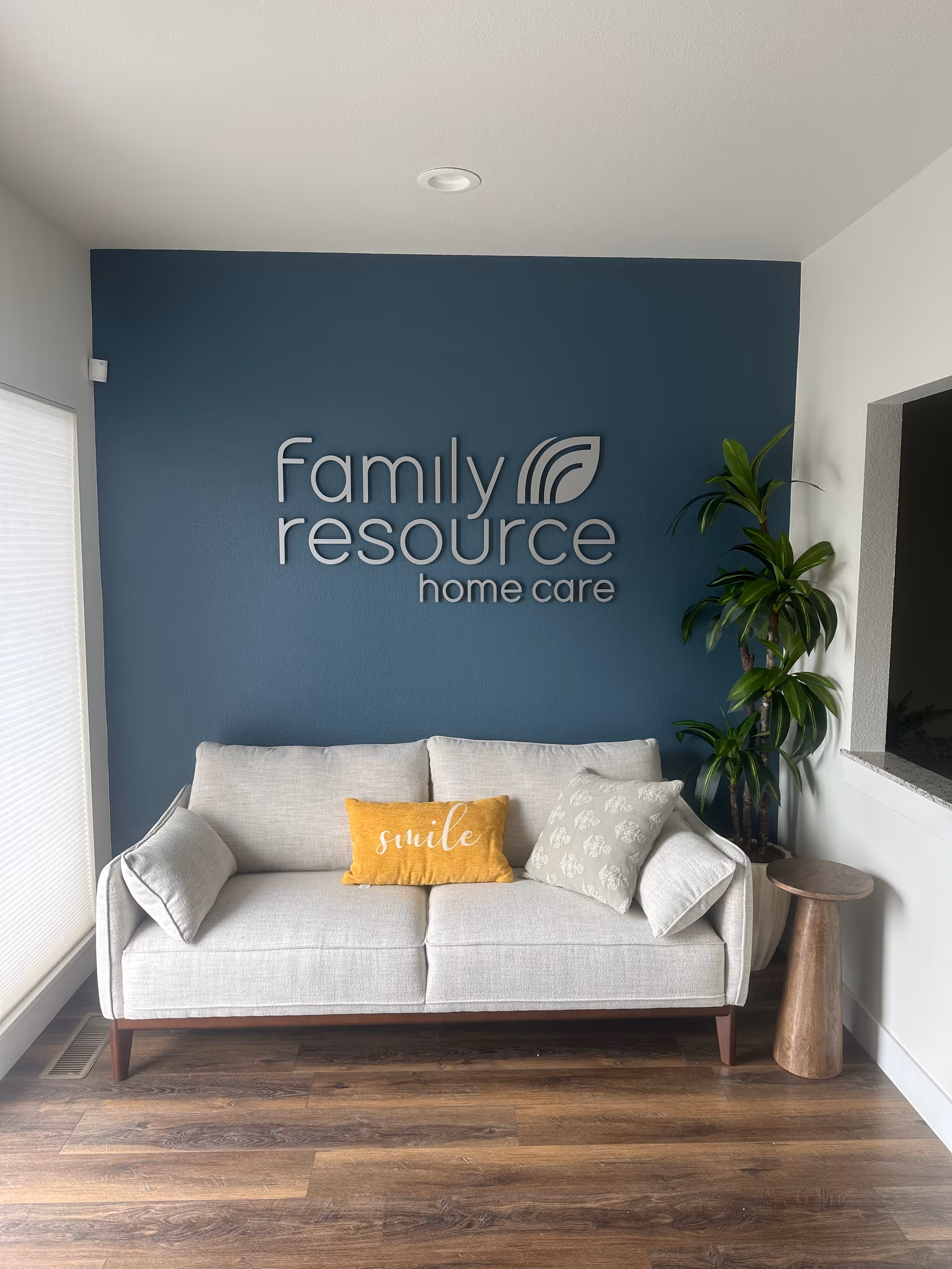 Lobby area with blue wall logo reading Family Resource Home Care, sofa, plant, and wood floor.