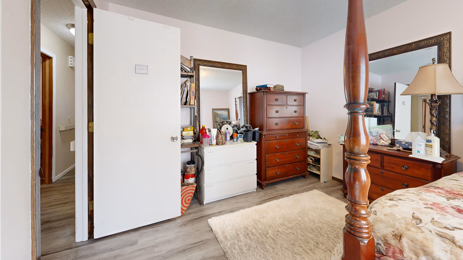 A cluttered bedroom with wood dressers, a four-poster bed, and mirrors.