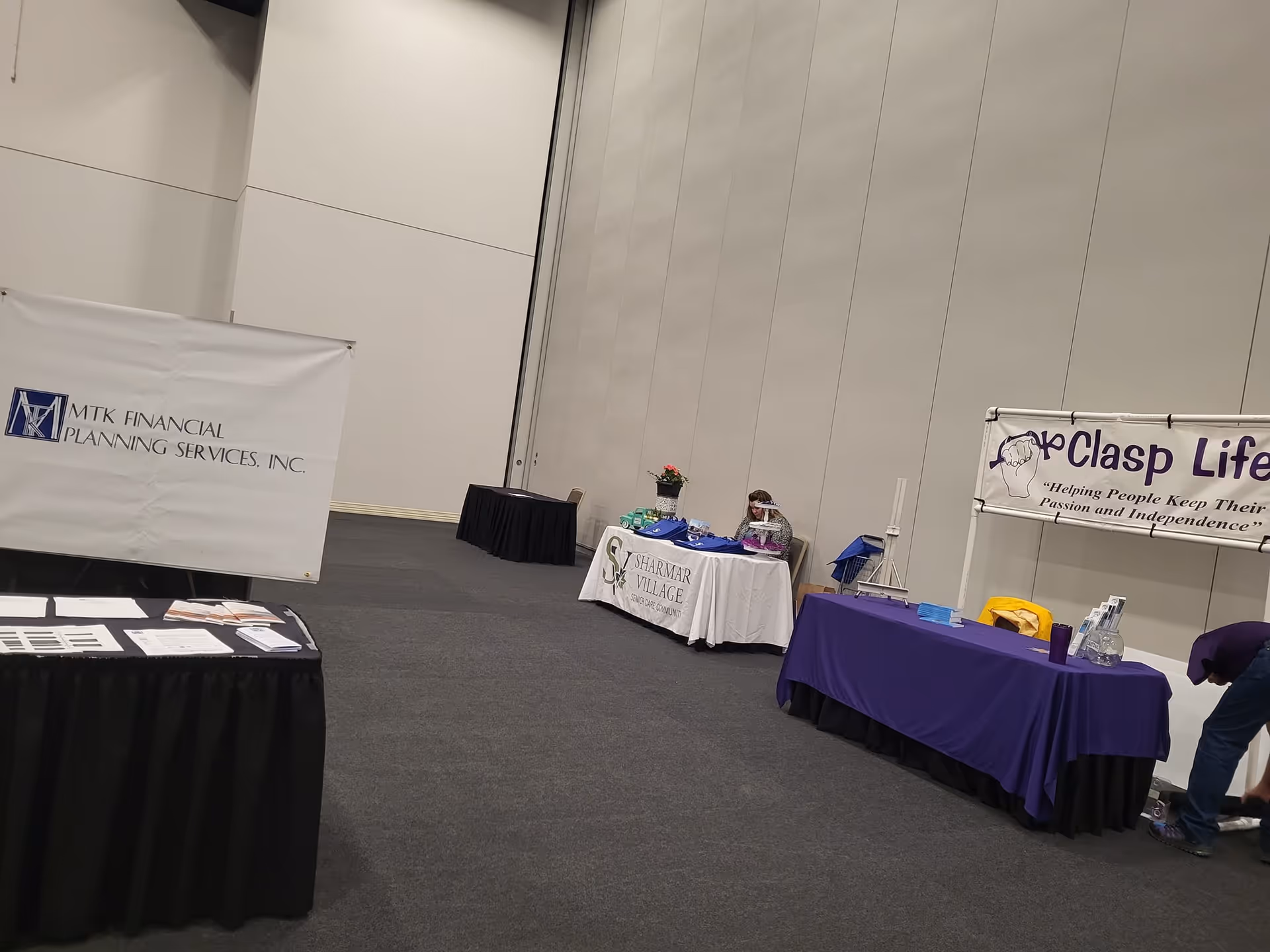Indoor convention hall with vendor tables, banners, and a person bending over on the right.