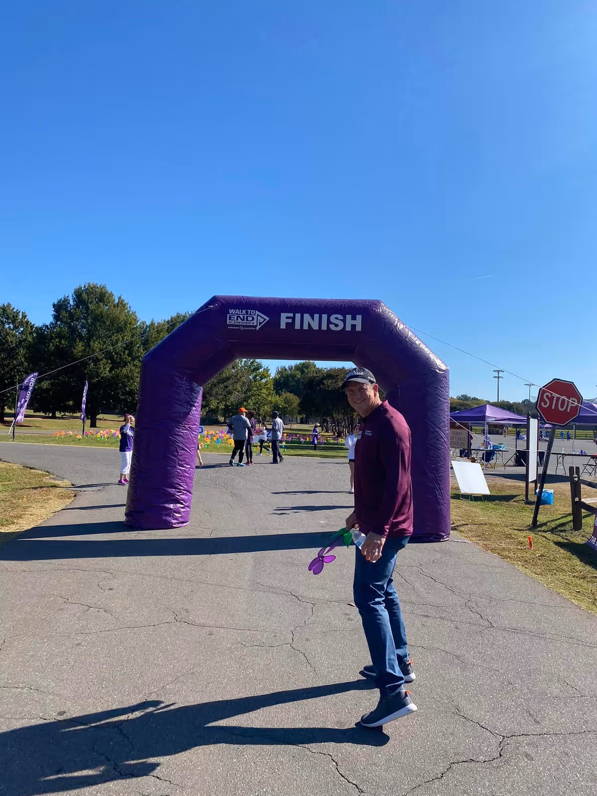 A man in a maroon shirt at a purple finish arch outdoors during an event.
