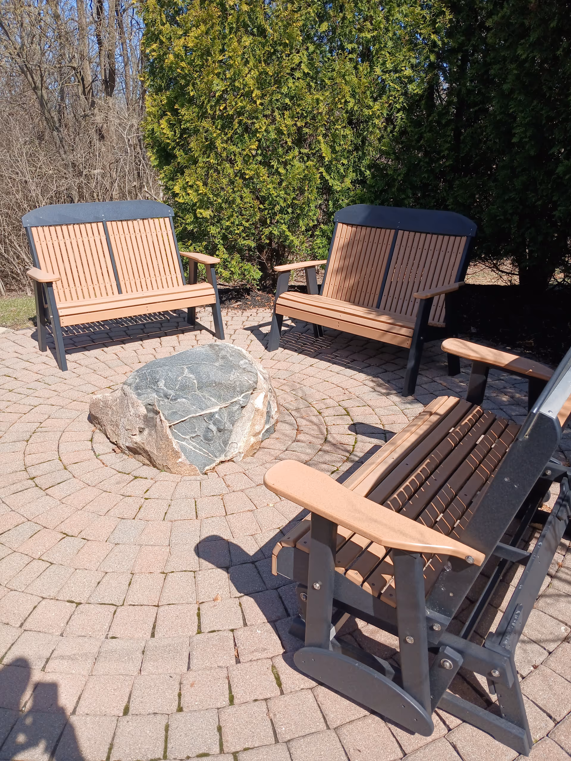 Outdoor seating area with wooden benches around a stone fire pit on a brick circle.