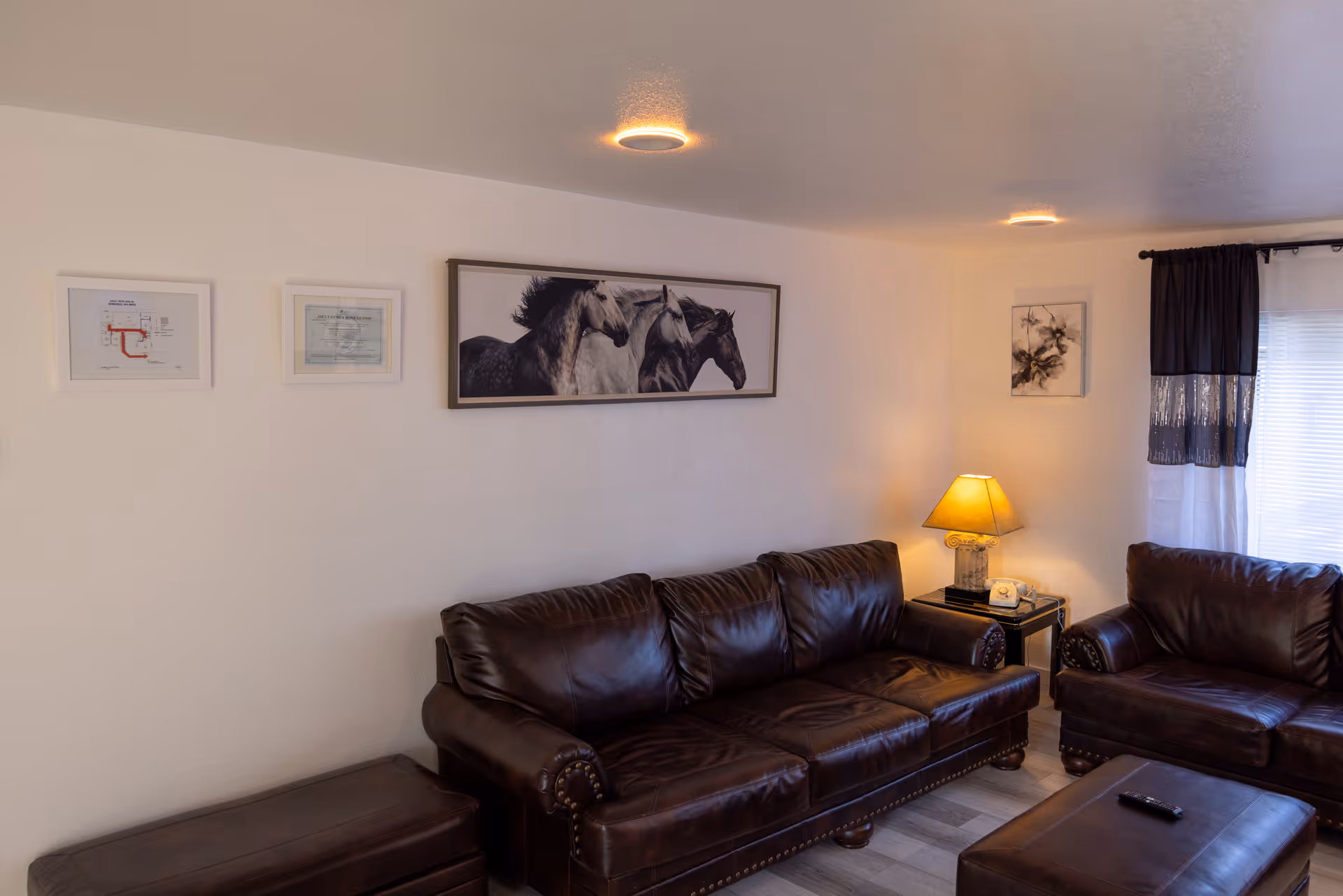 Cozy living room with dark leather sofas, coffee table, lamp, and horse artwork.