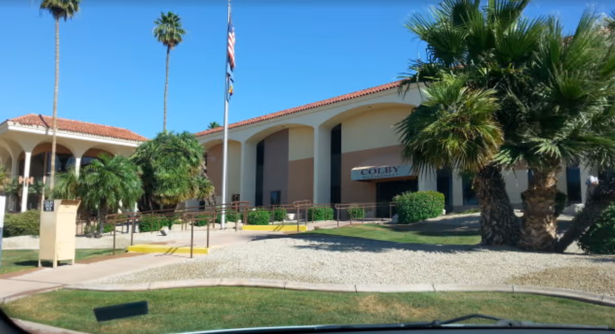 Exterior view of a senior care facility with palm trees, flags, and a curved entrance.