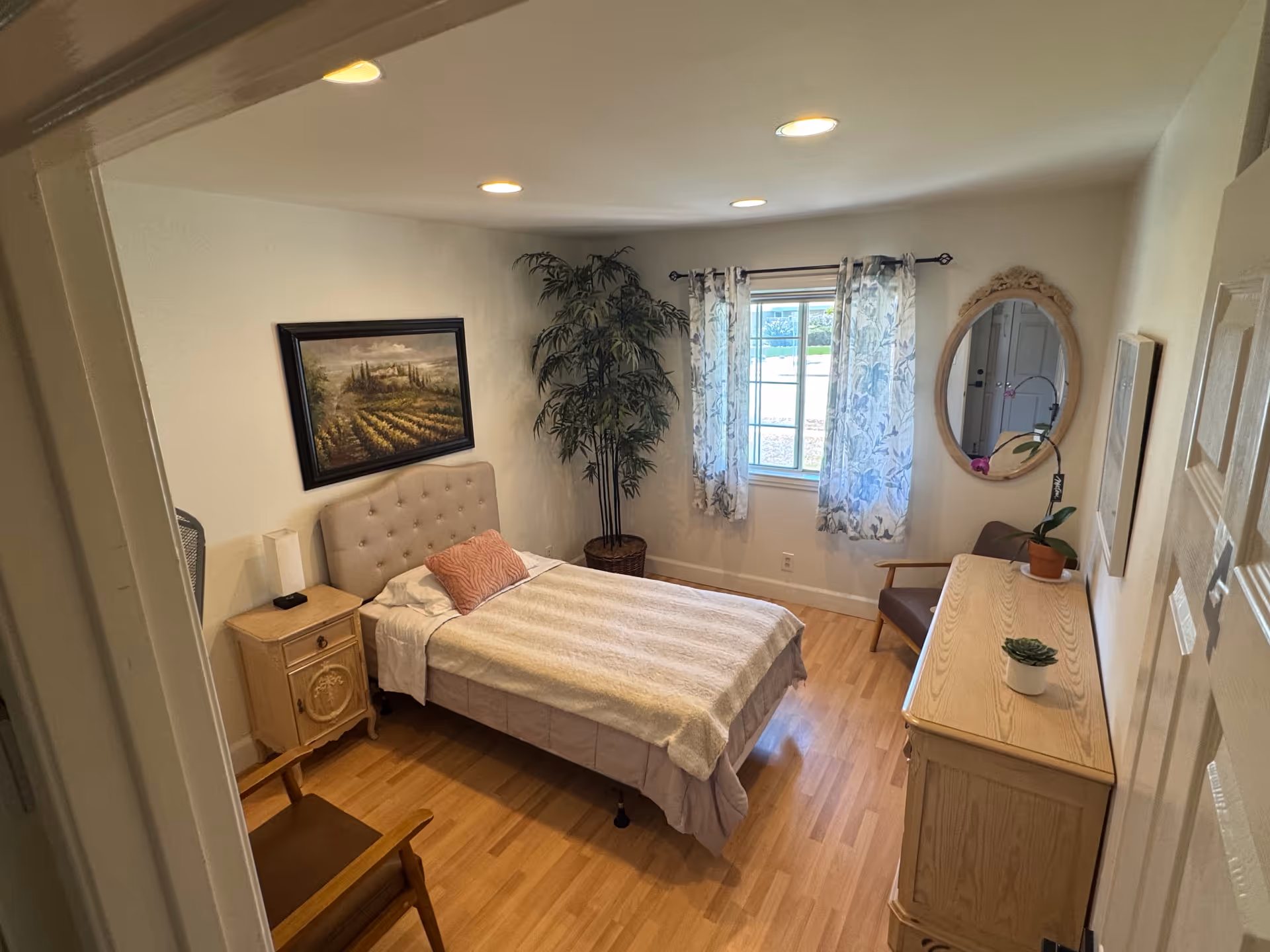 Cozy bedroom in a senior living facility featuring a bed, dresser, window, and plant.