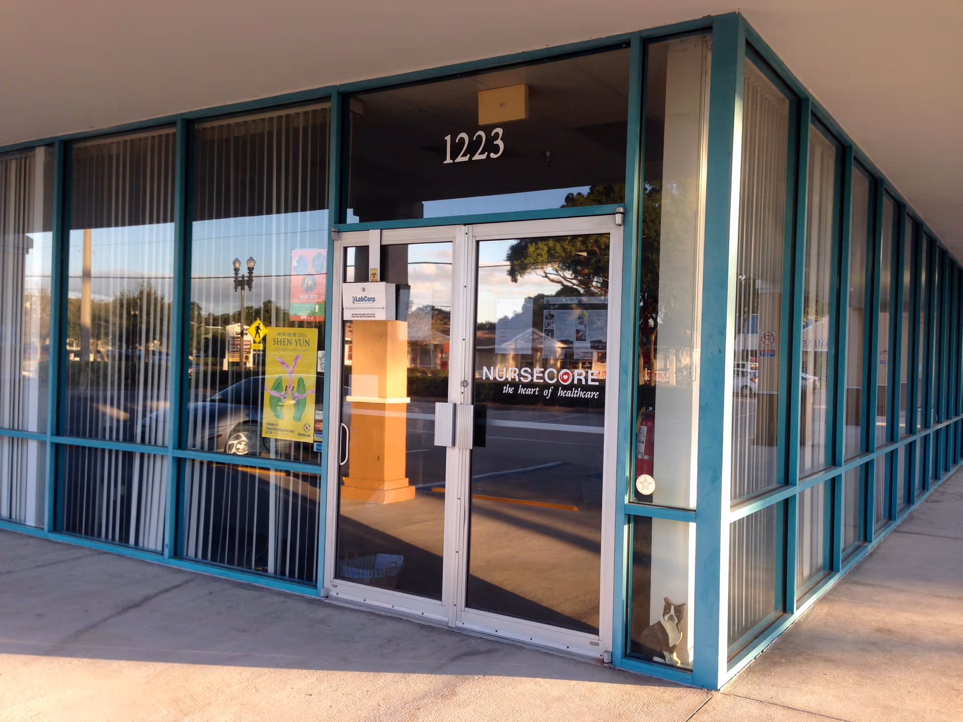 Exterior view of NurseCore facility entrance with glass doors, teal framing, and the number 1223.