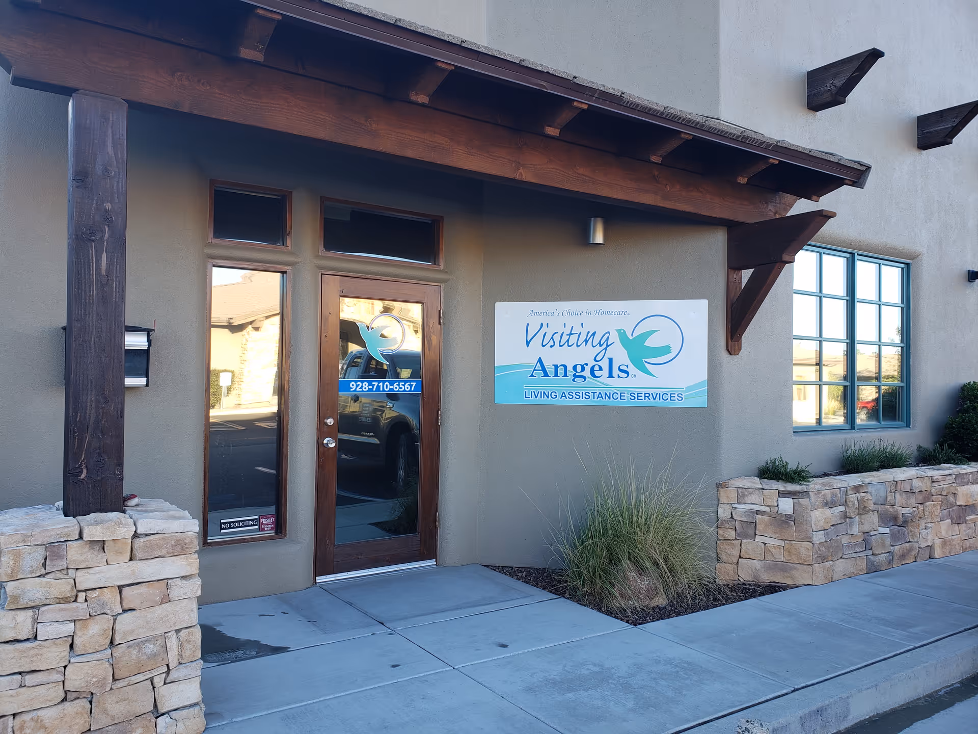Exterior view of Visiting Angels facility entrance with door, window, sign, and stone landscaping.