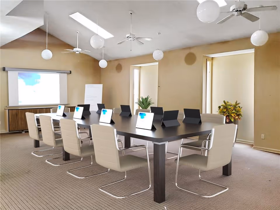 A spacious conference room in a senior living facility with a long table and tablets.