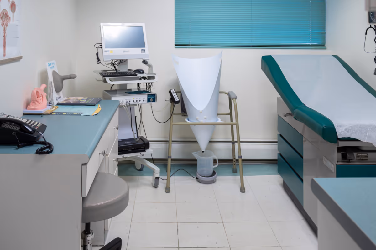 Medical examination room with monitor, cart, cone device, and teal examination bed.