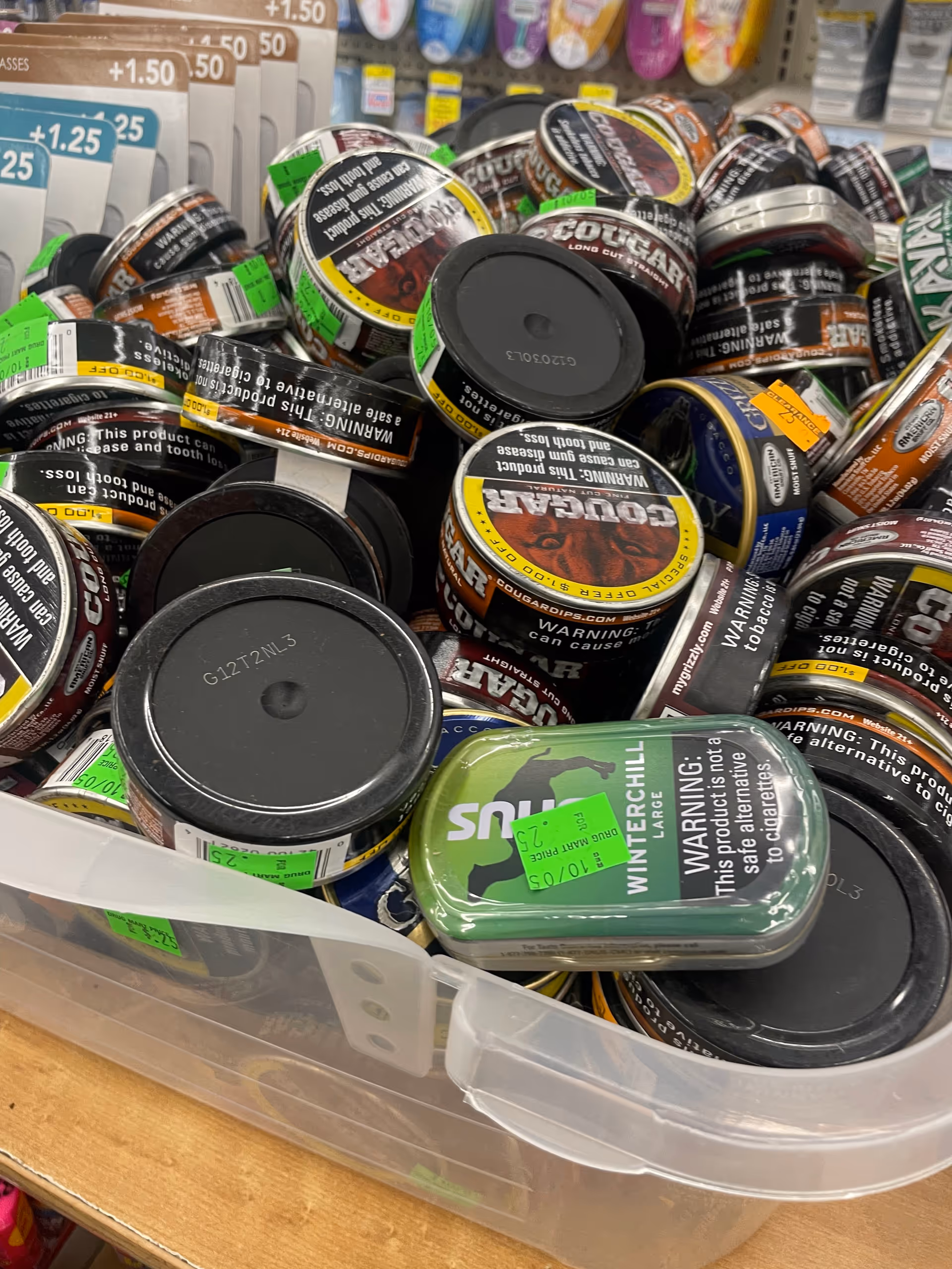 Close-up view of assorted tobacco tins piled in a plastic bin at a store.
