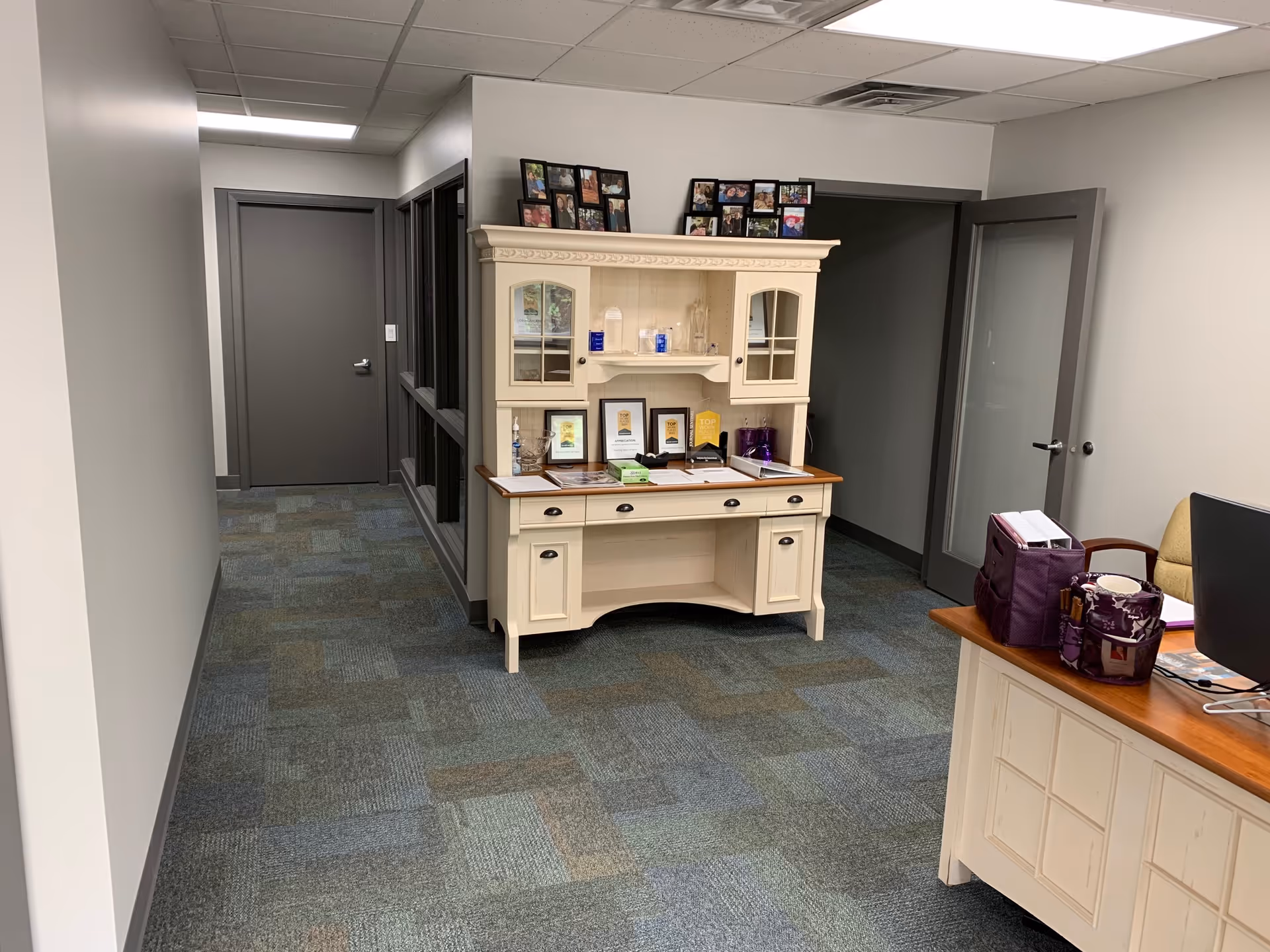 Hallway with cream reception cabinet, framed photos, and a desk in a facility interior.