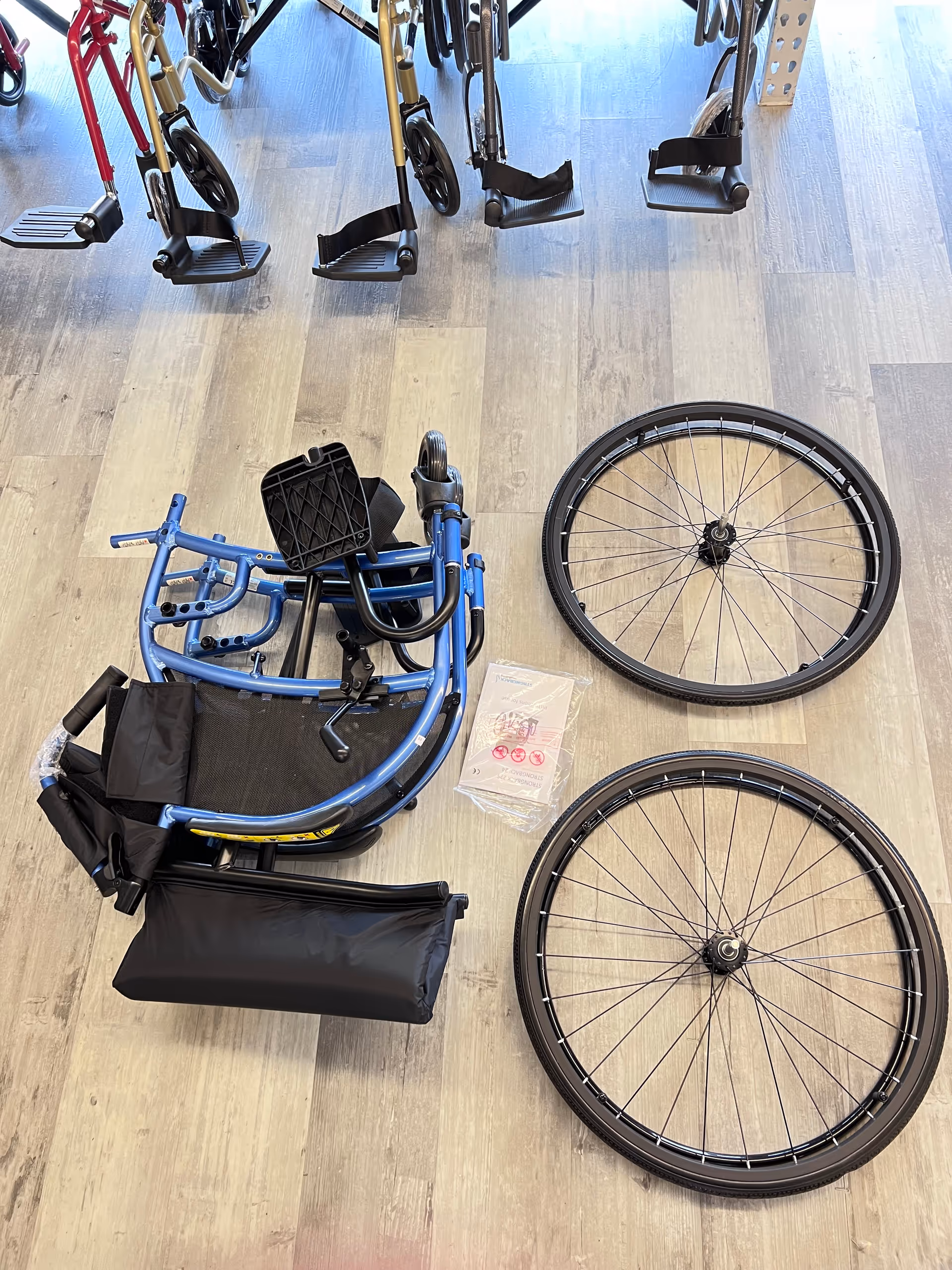 Blue foldable wheelchair on a wooden floor among walkers in interior facility.