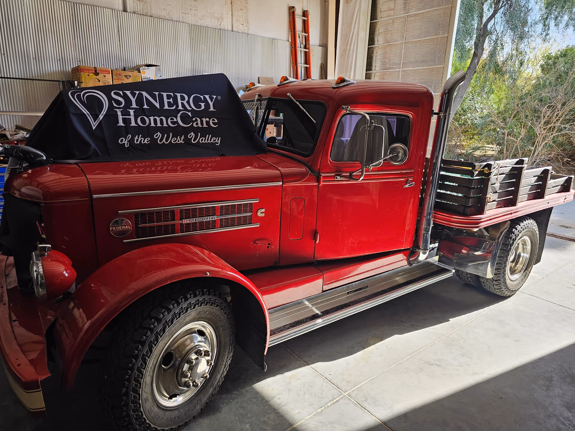 Red vintage truck with SYNERGY HomeCare banner parked inside a garage.