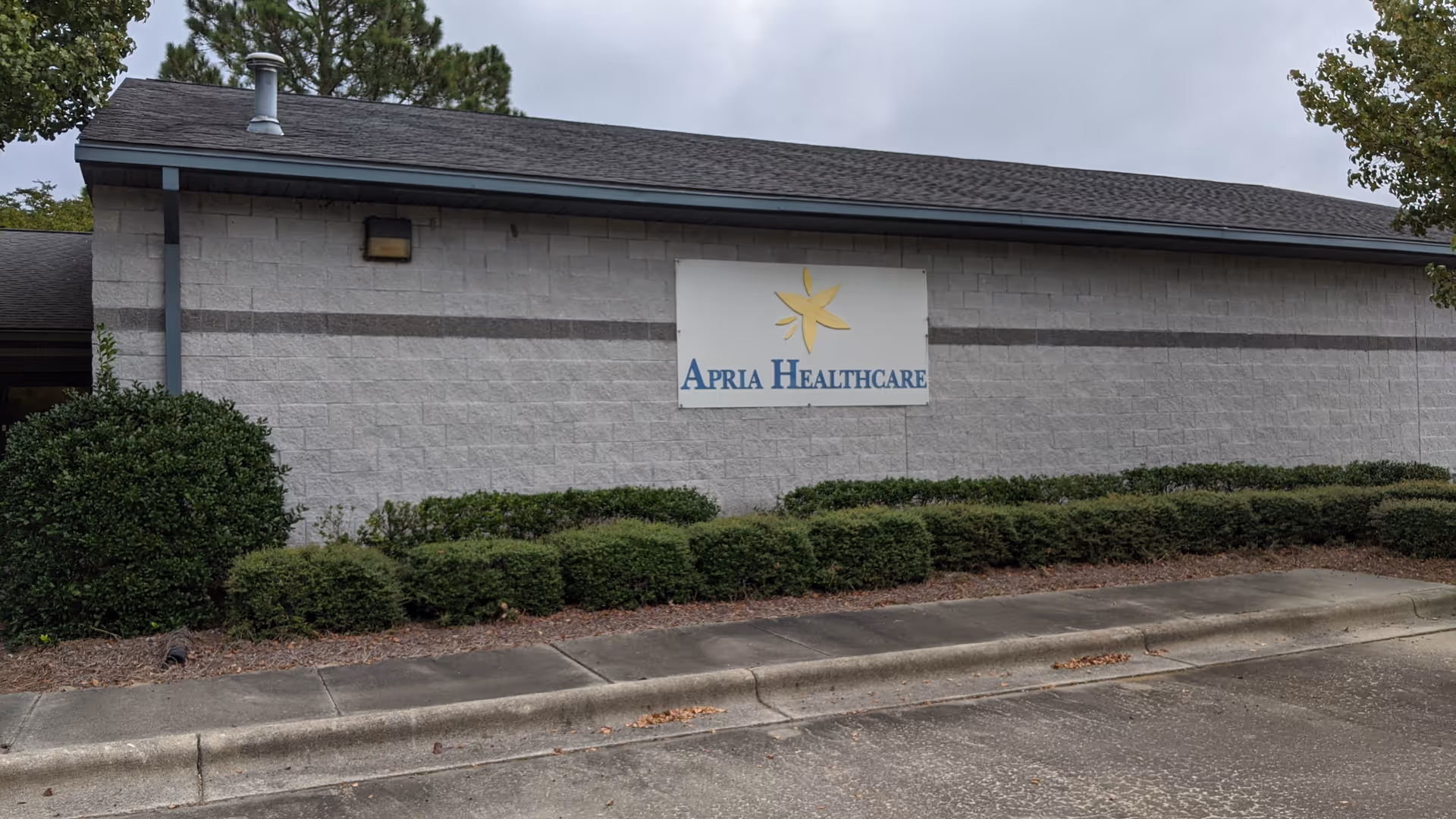 Exterior view of Apria Healthcare building with sign and landscaped shrubs.