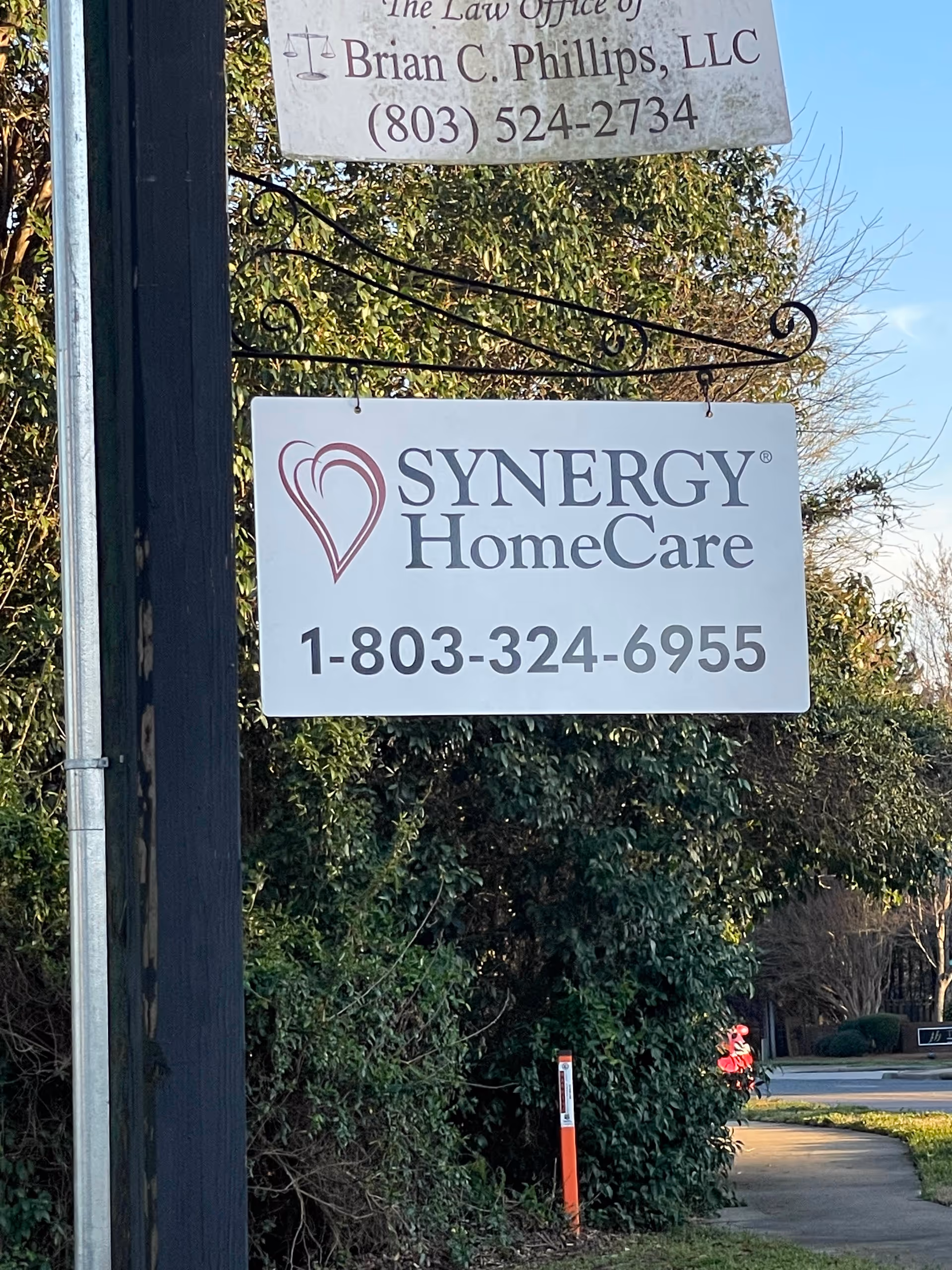 Outdoor hanging sign displays Synergy HomeCare logo and contact number.