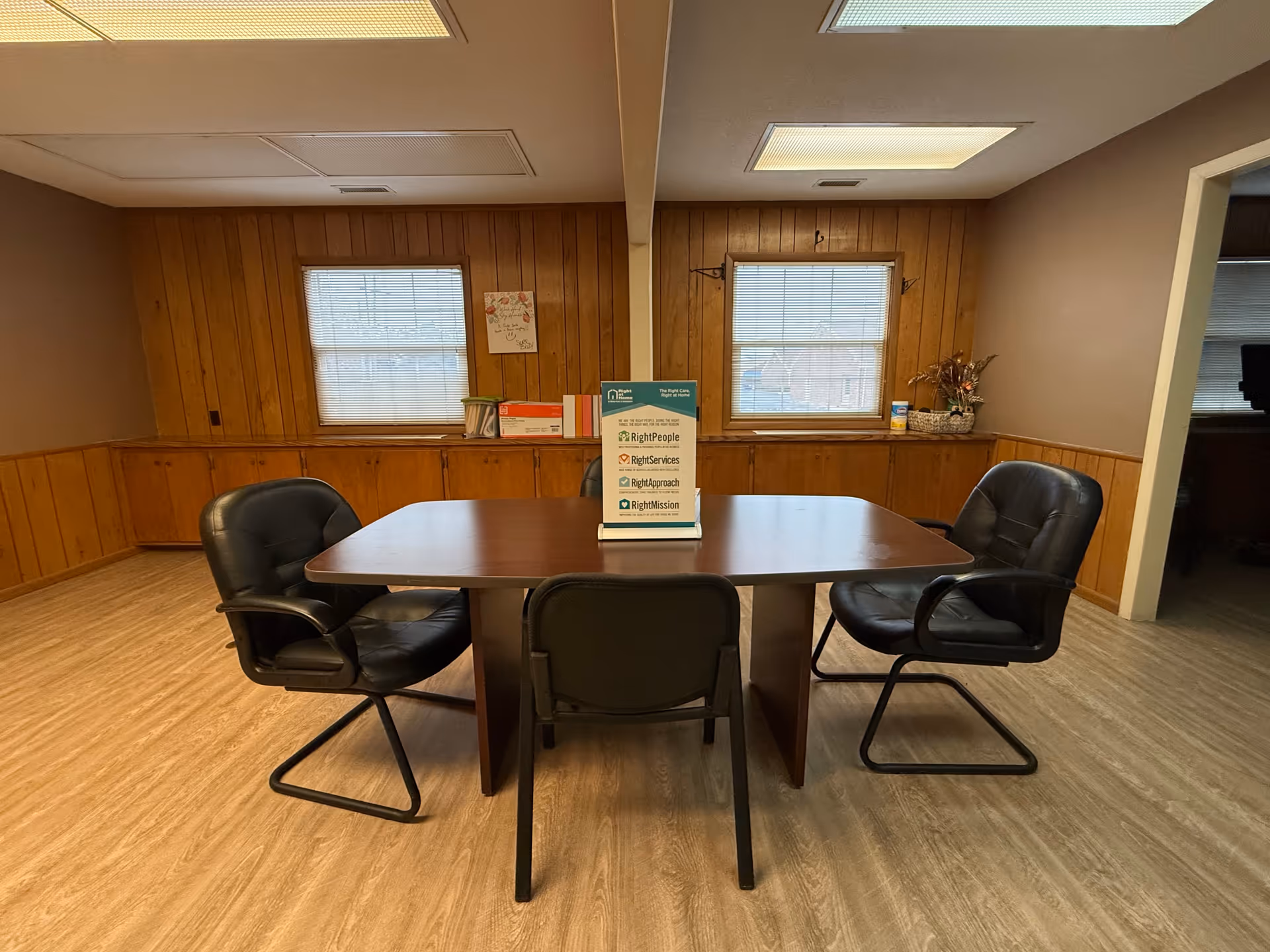 A conference-style meeting room with a wooden table and four black chairs.