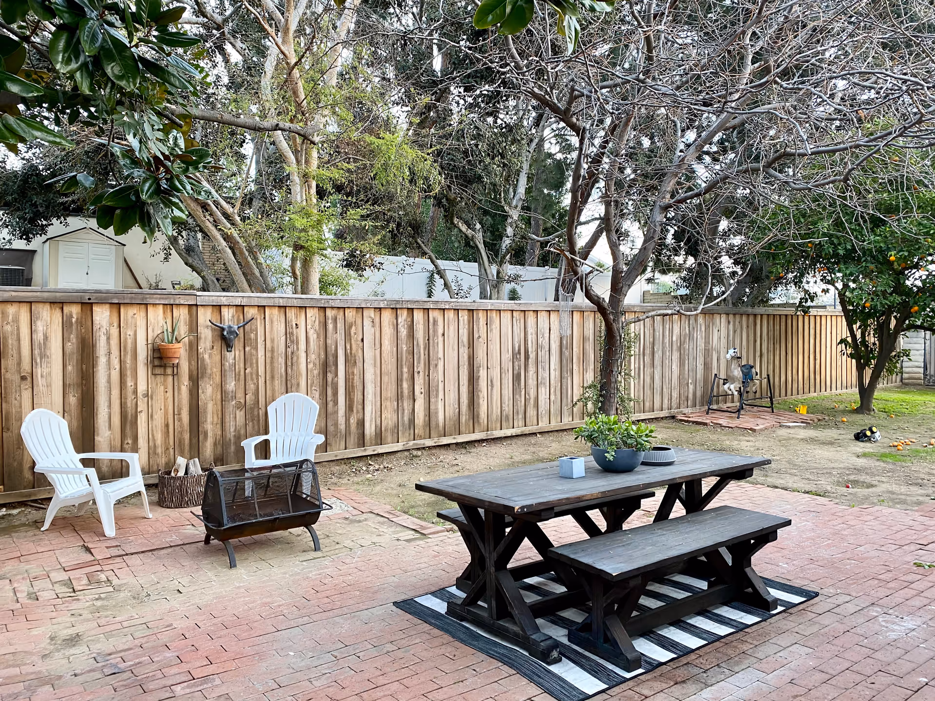 Backyard patio with a wooden fence, picnic table, benches, and white plastic chairs.