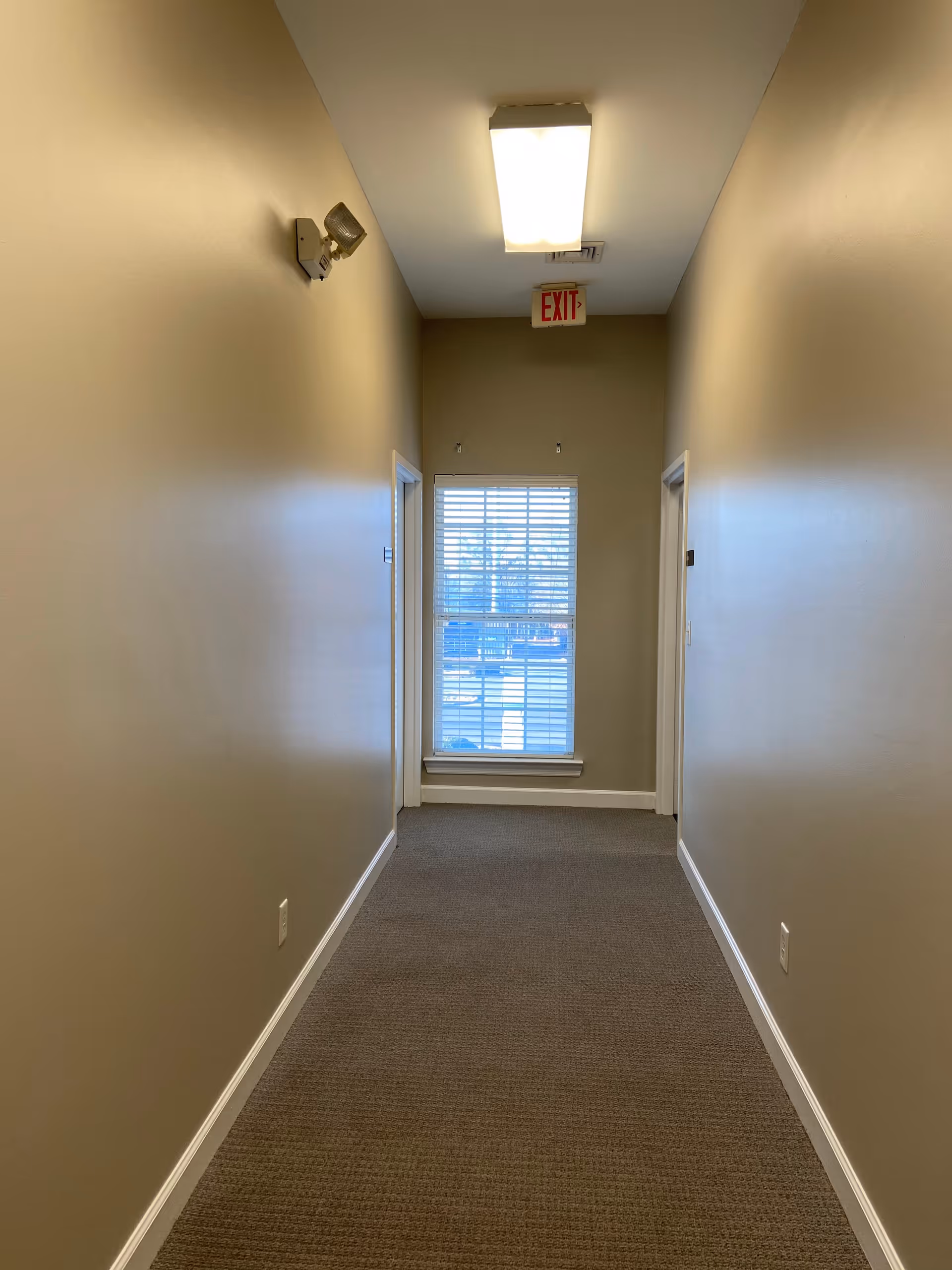 Long beige hallway in a senior living facility with a lit ceiling, exit sign, and window.