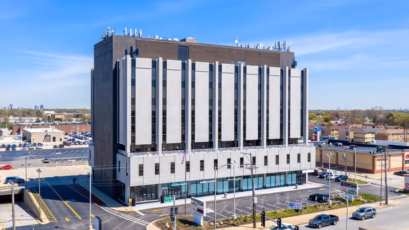 Exterior view of a tall, modern building with a parking lot under blue sky.