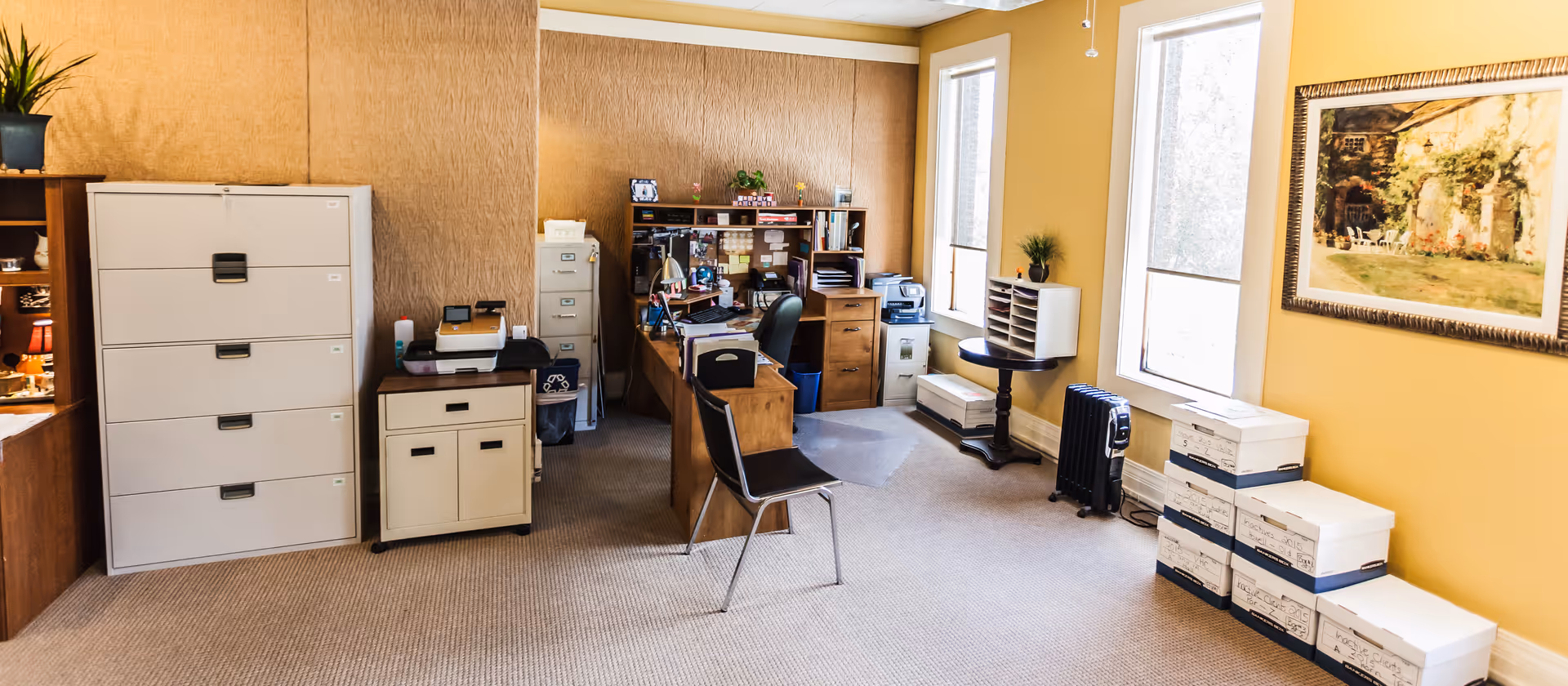 Administrative office area with desks, filing cabinets, and stacked boxes in a senior facility.