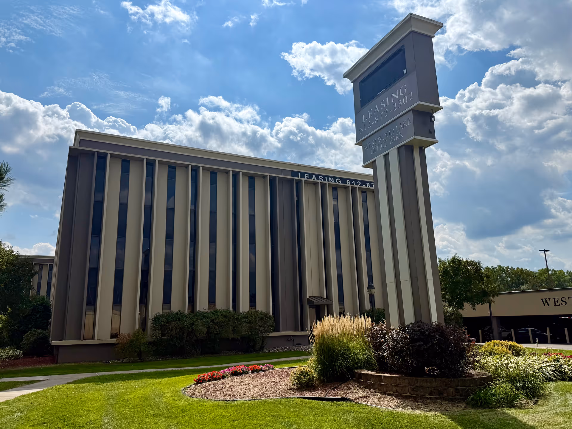 Modern facility exterior with tall sign and landscaped entrance under a blue sky.