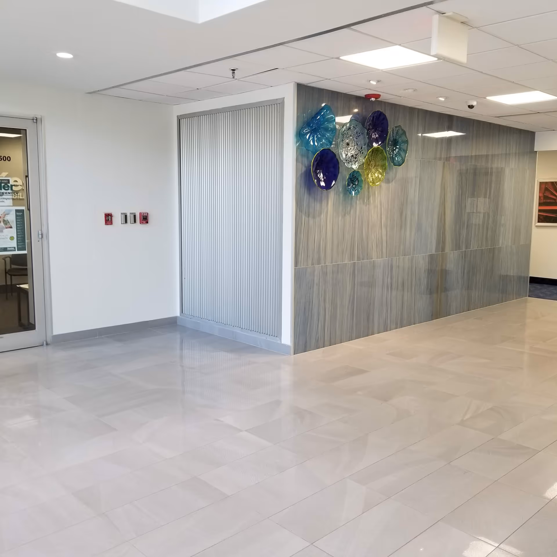 Bright interior hallway with glossy tile floor, glass wall art, and doorway.