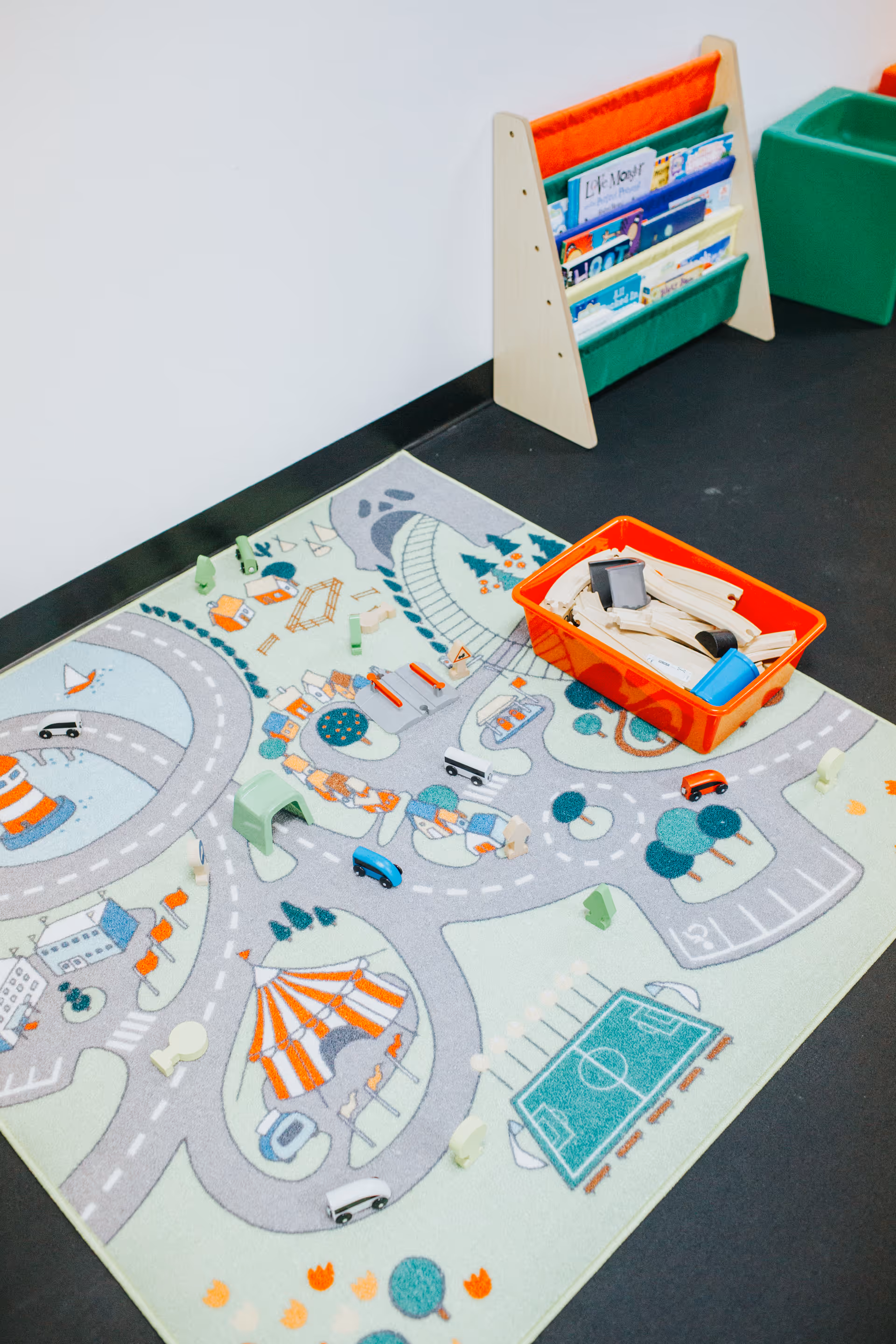 Colorful play mat with toy cars, a red bin, and a bookshelf in a play area.