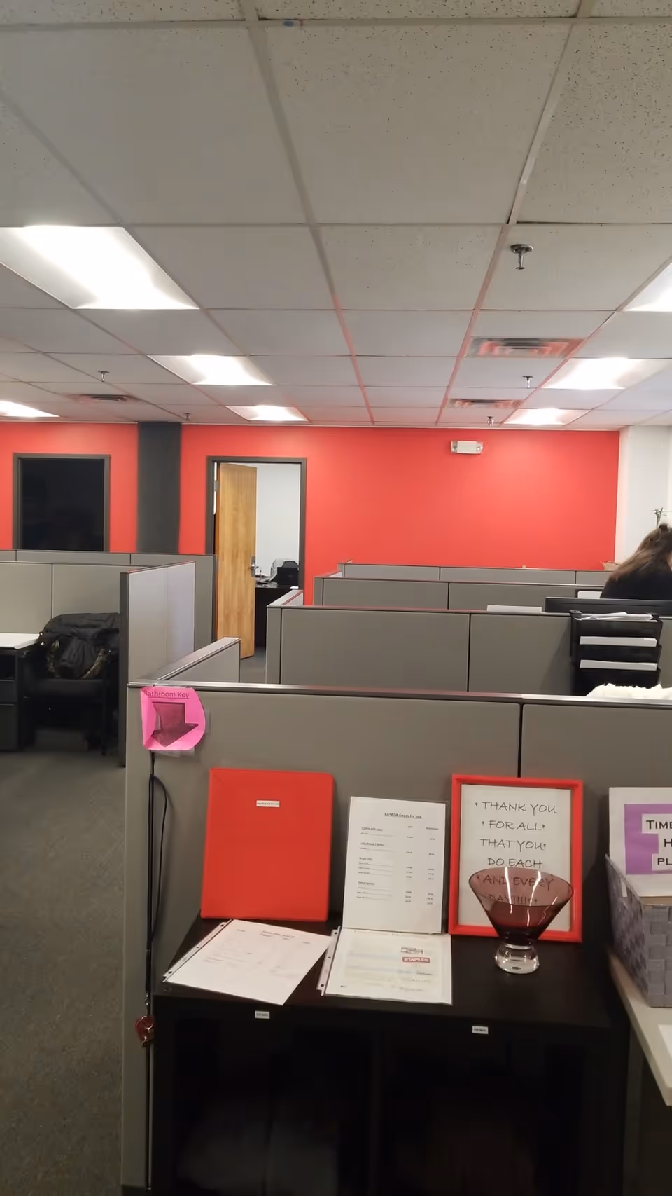 Interior view of office cubicles with a red accent wall and scattered documents.