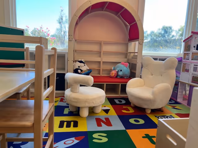 Colorful indoor play area with small chairs, stuffed animals, and an alphabet rug.