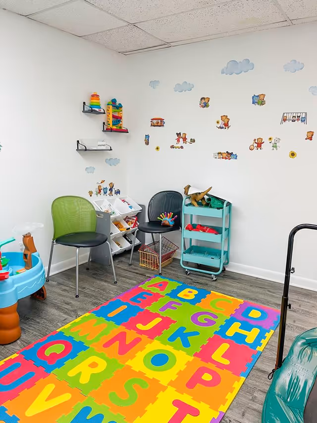Bright indoor playroom with colorful alphabet mat, toys, and wall decals.