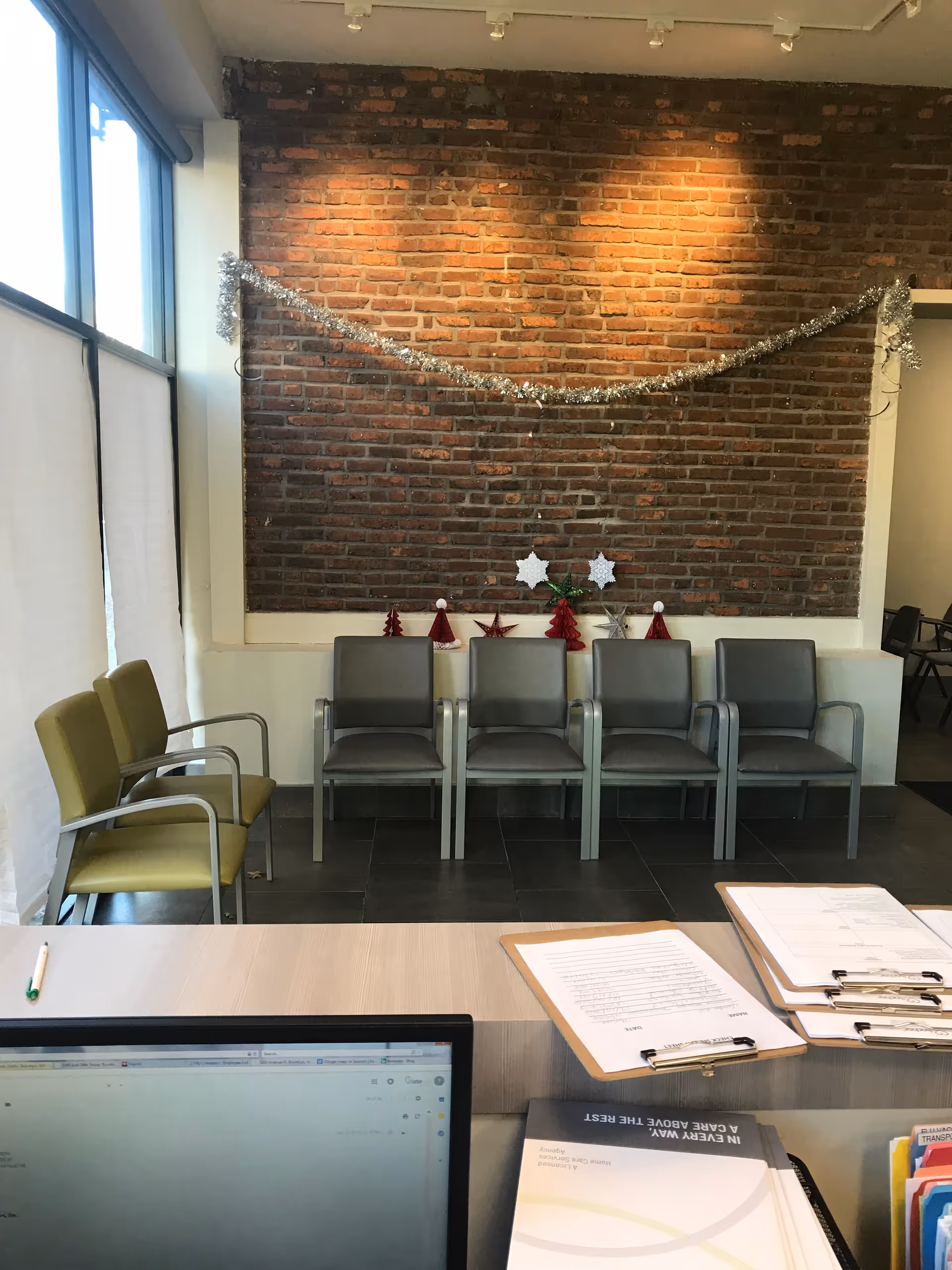 Interior reception area with brick wall, garland, row of chairs, and desk with documents.