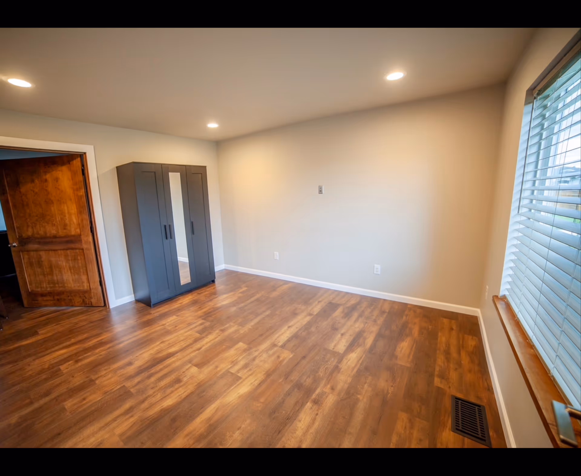 Empty interior room with hardwood floor, gray wardrobe, and window blinds.