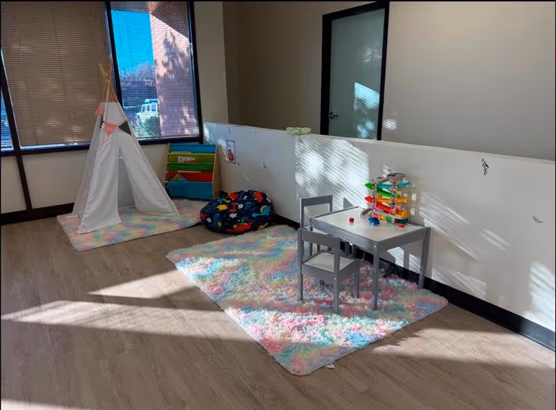 Indoor play area with a teepee tent, colorful rug, cushions, and a small table with toys.