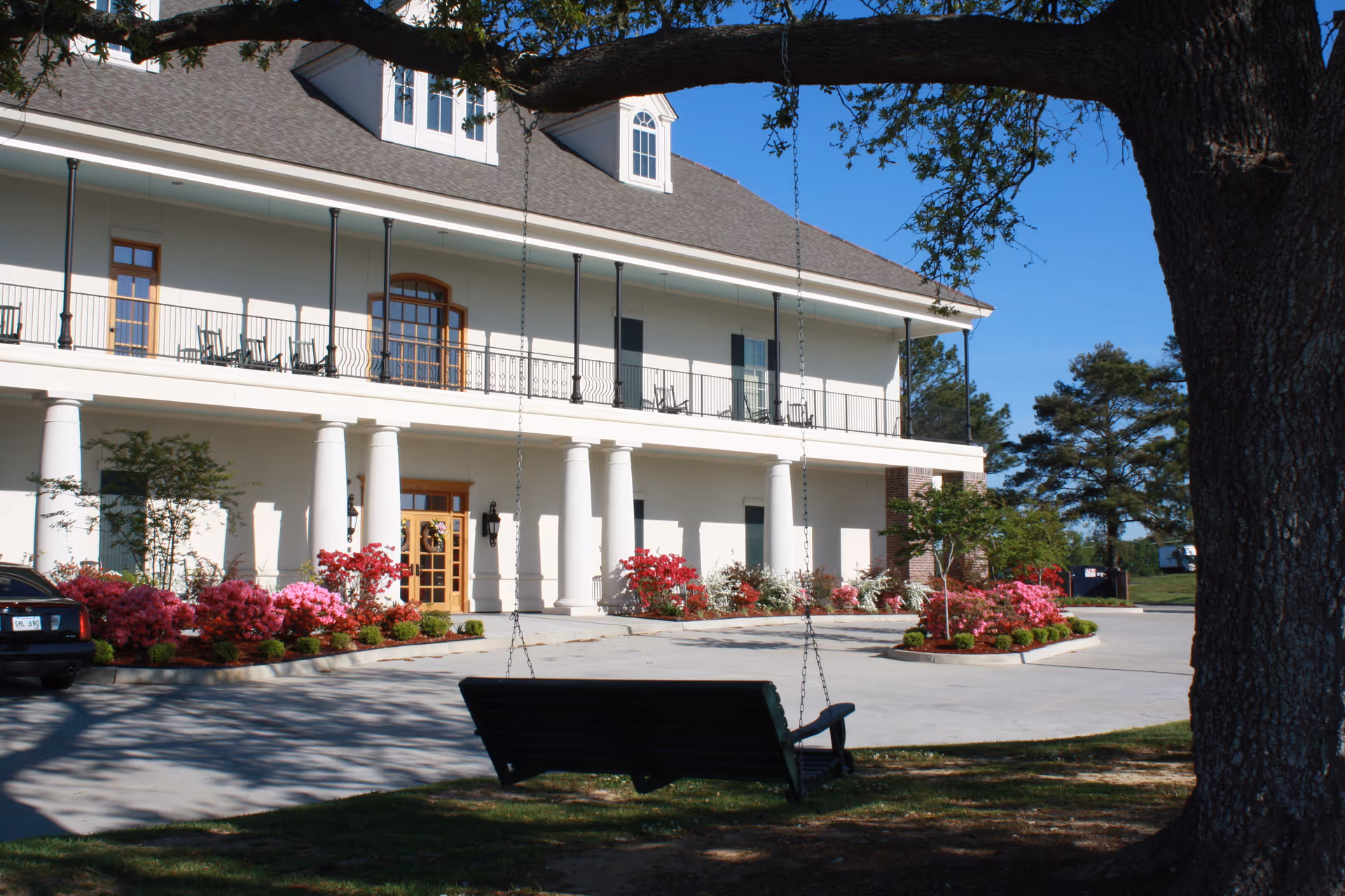 Exterior view of a white, columned senior living building with a swing bench and landscaping.