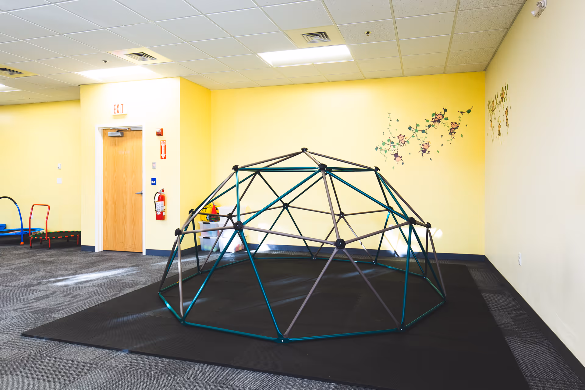 Indoor play area with a geodesic climbing dome against yellow walls.