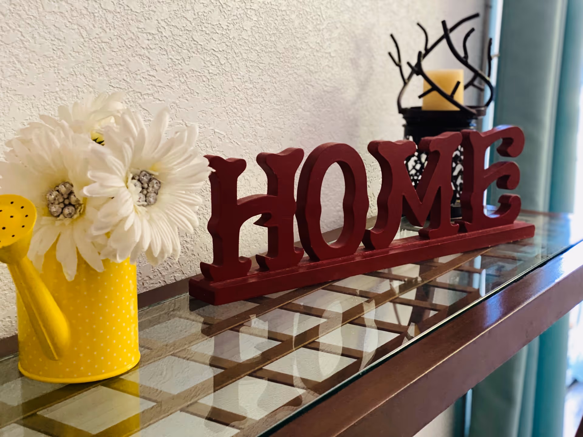 Decorative countertop with a yellow polka-dot watering can, white flowers, and a red HOME sign.