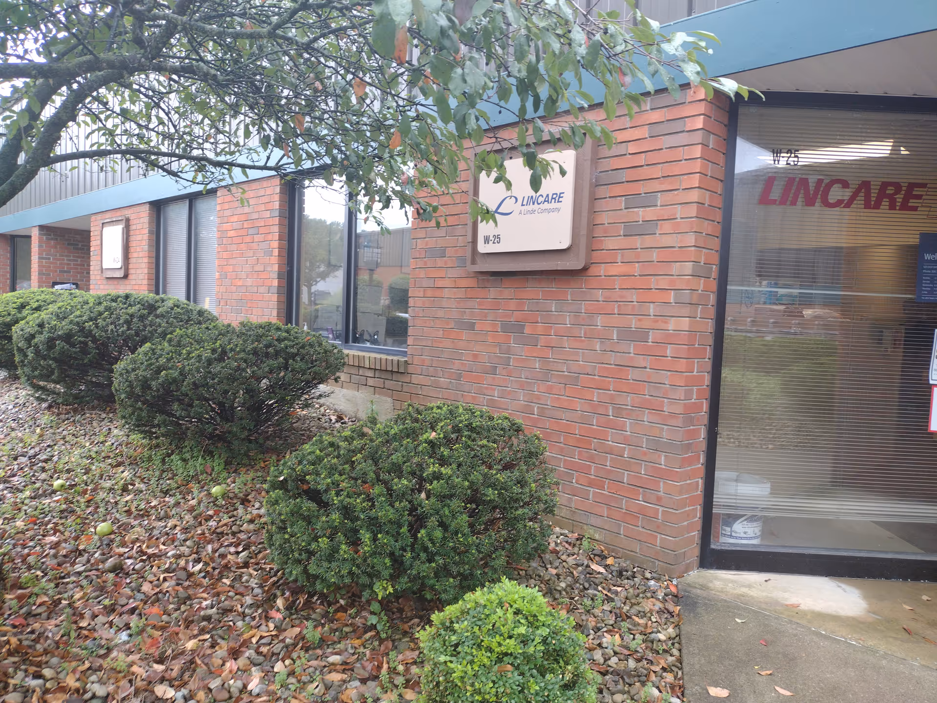 Brick exterior of LINCARE facility with sign, windows, and shrubs.