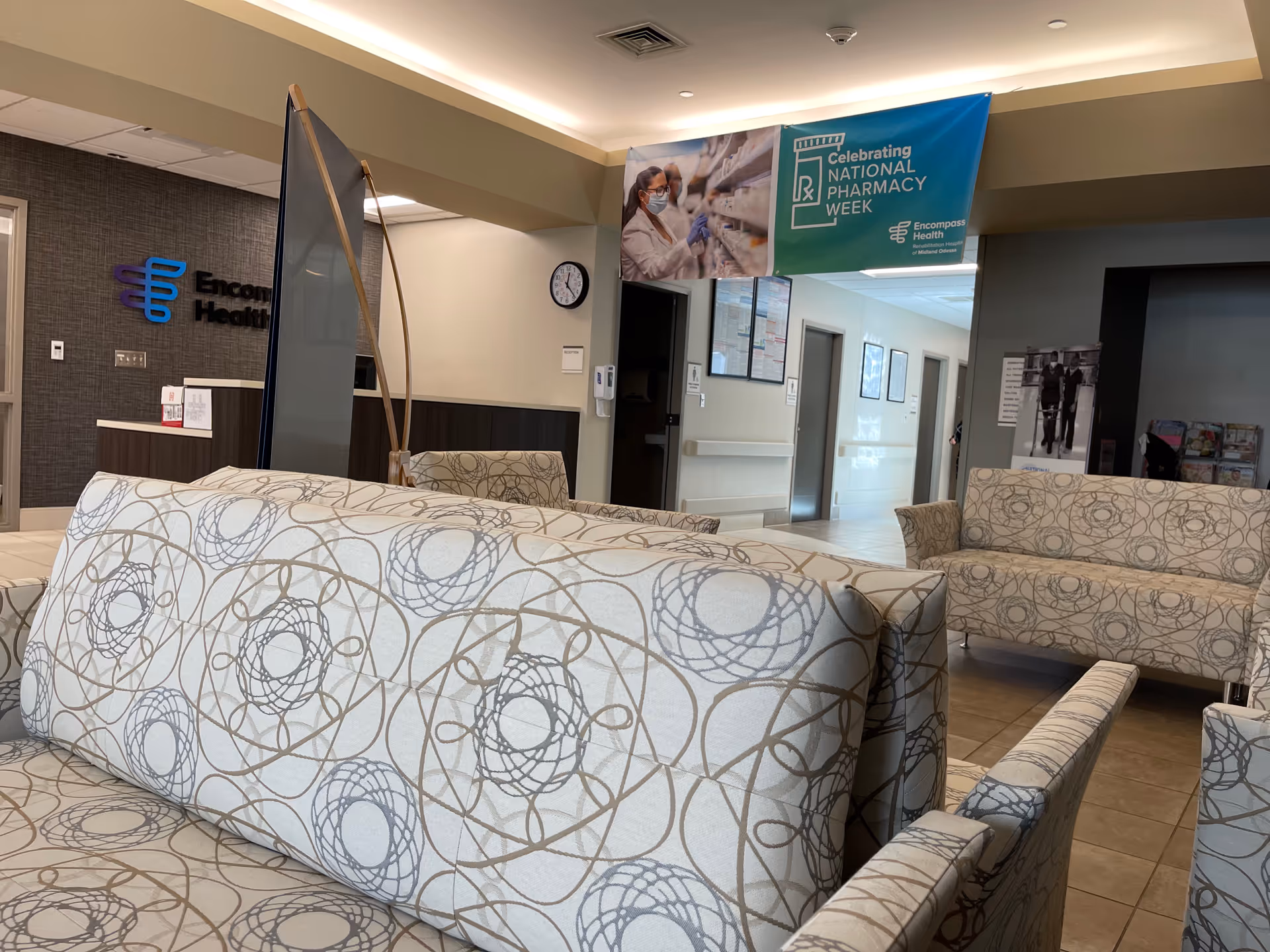 Facility lobby with patterned beige seating, a reception desk, and a blue banner.