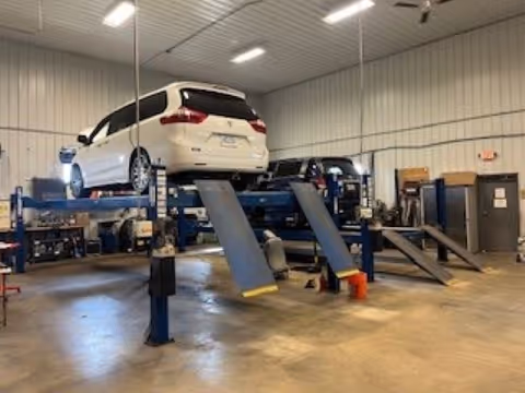 White SUV elevated on a vehicle lift inside a spacious automotive workshop with tools and equipment.