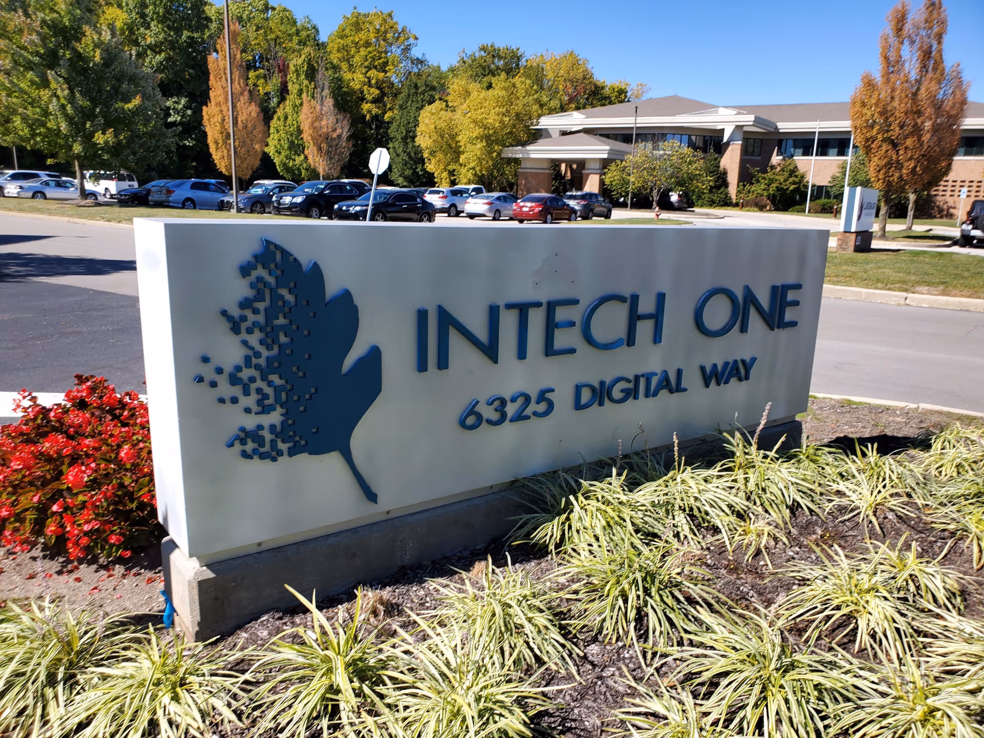 Large sign reading INTECH ONE with a leaf logo, surrounded by landscaping and a distant building.