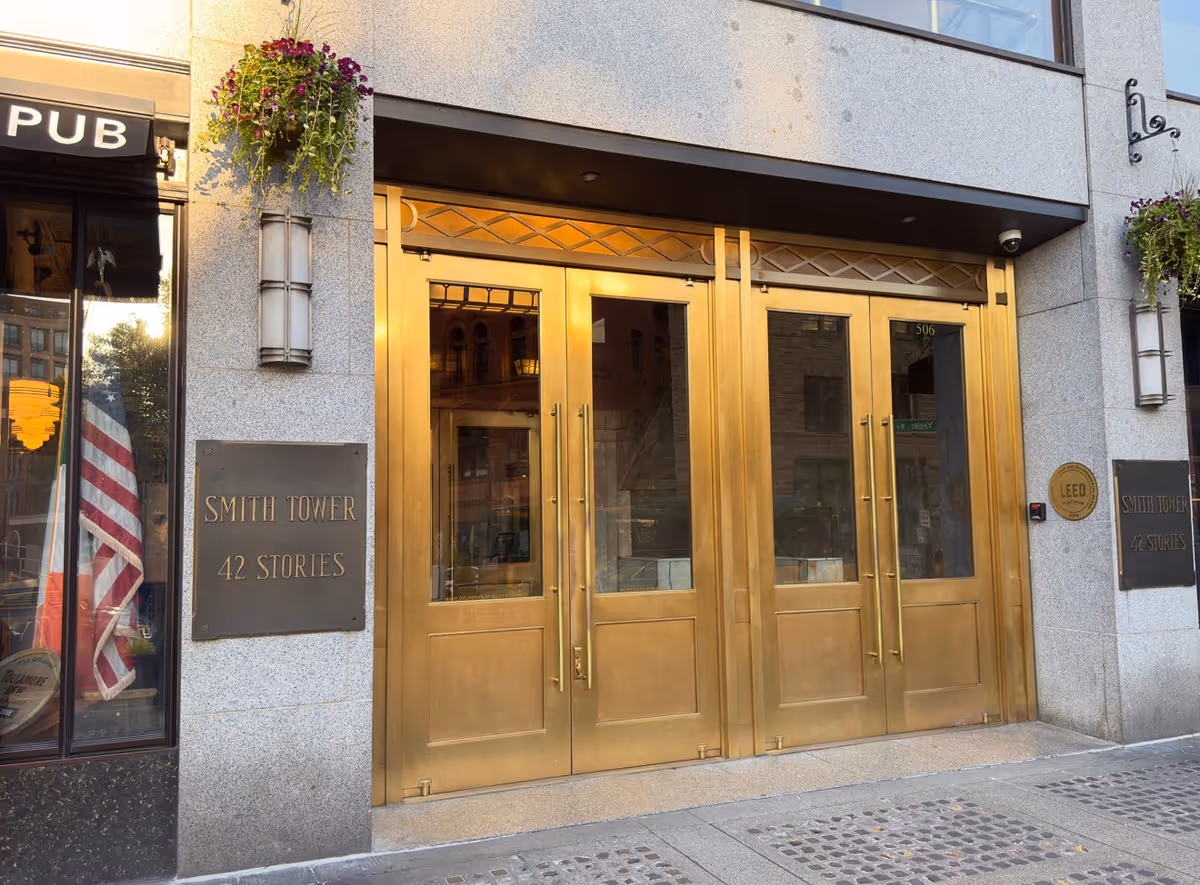 Gold entrance doors of a tall building with Smith Tower signage and US flag visible.