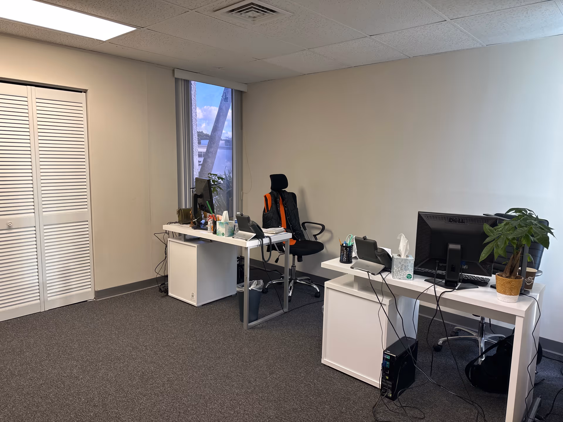 Two white desks with computers and a plant in a small, tidy office.