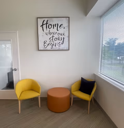 Bright indoor lounge area with two yellow chairs, a brown ottoman, and wall art.