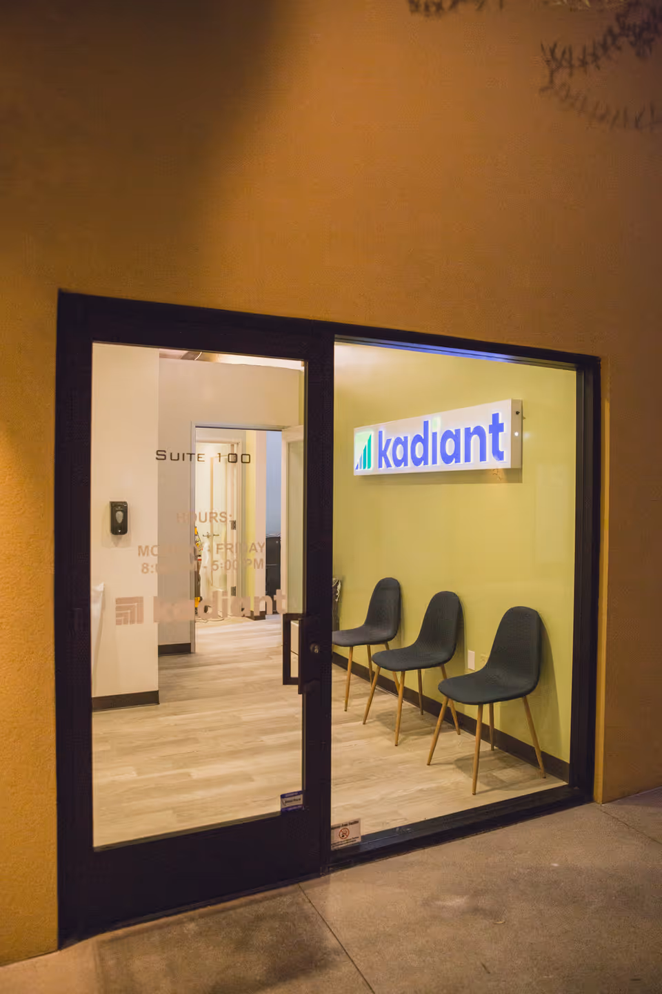 Glass doors open to a lobby with three chairs and a Kadiant sign.