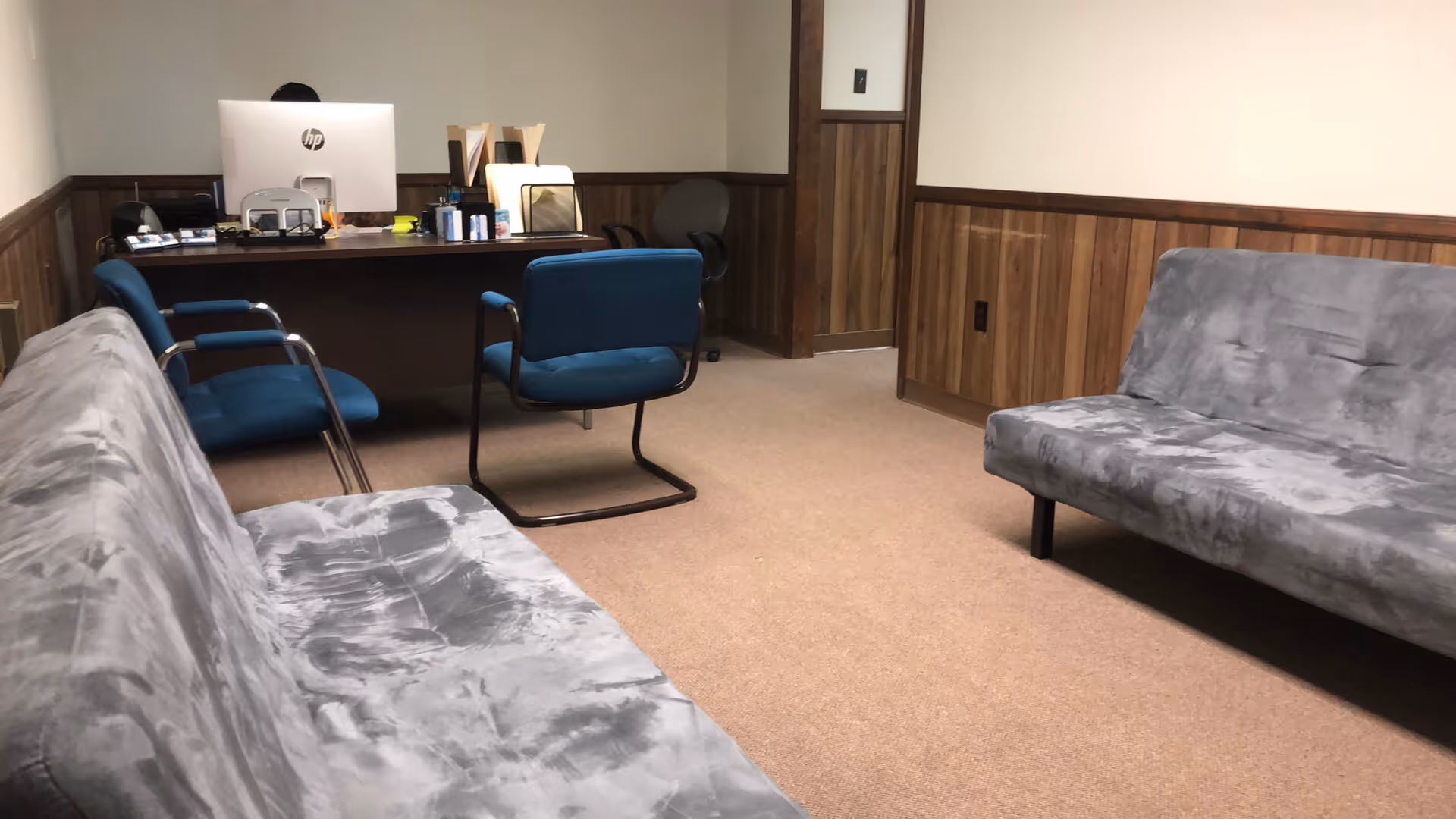 Office reception area with blue chairs, desk, computer, and gray couches.