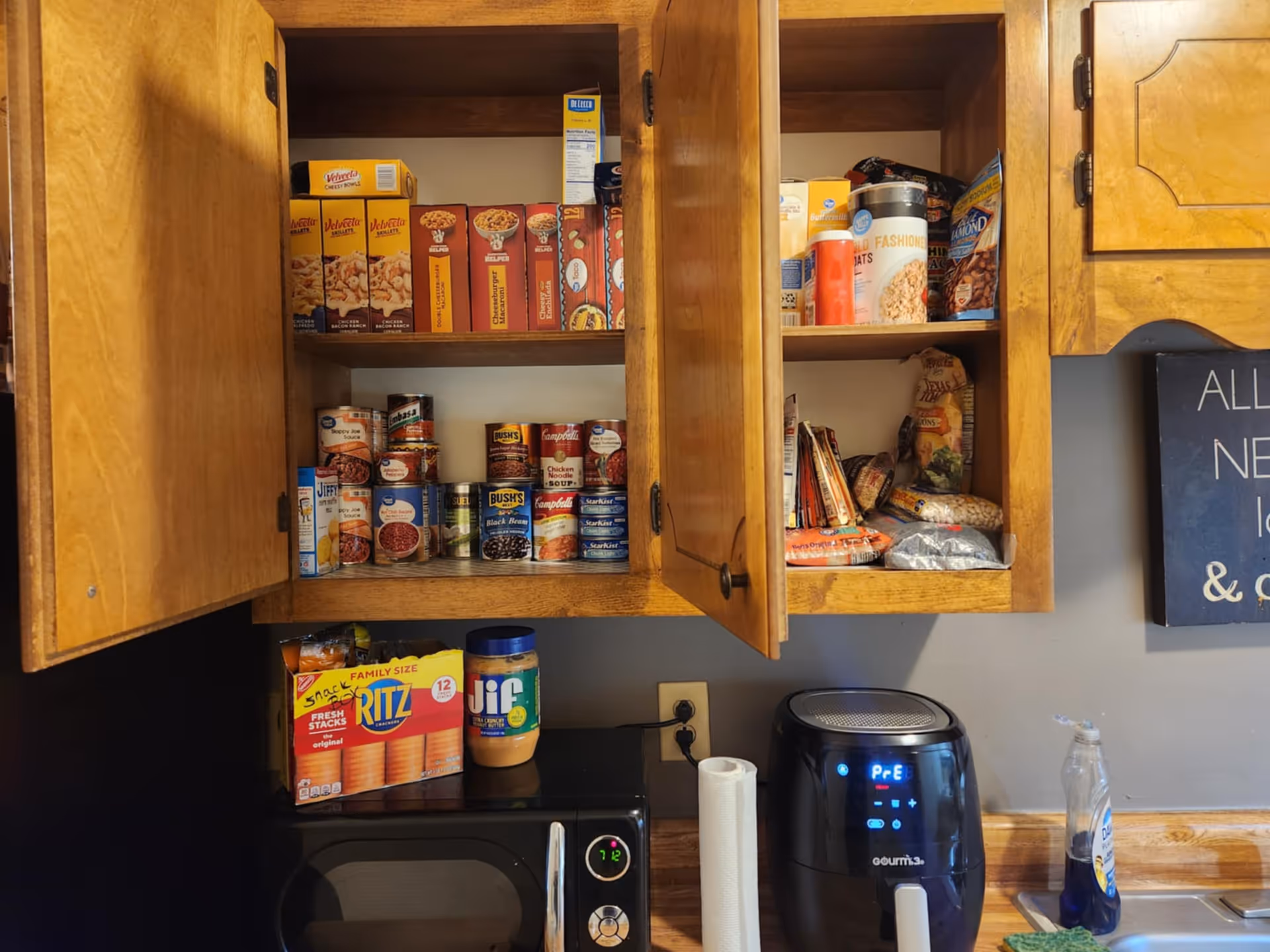 Open kitchen cabinets with boxed cereals, canned goods, a microwave, and an air fryer.