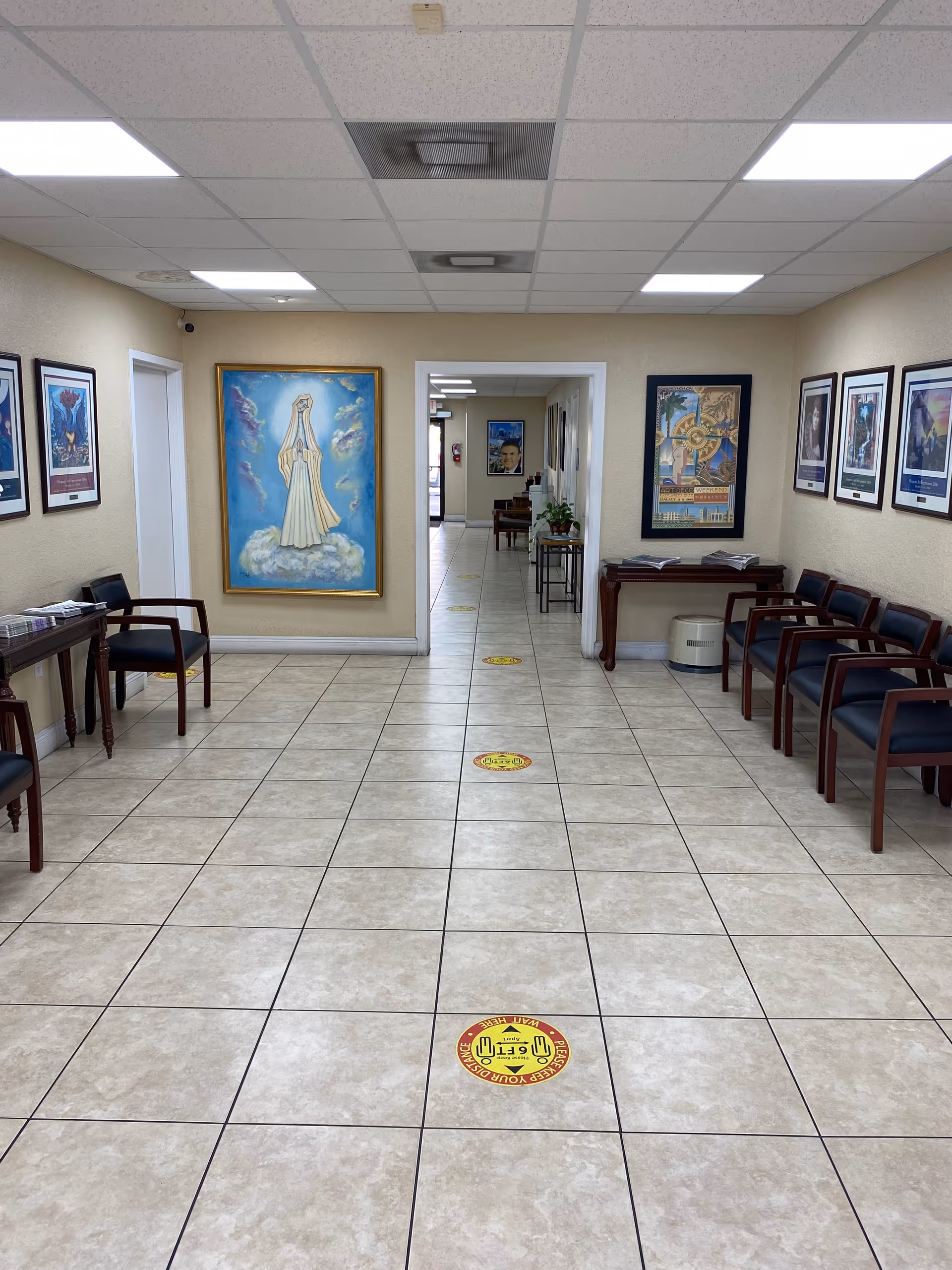 Wide tiled hallway in a senior living facility with framed art and chairs.