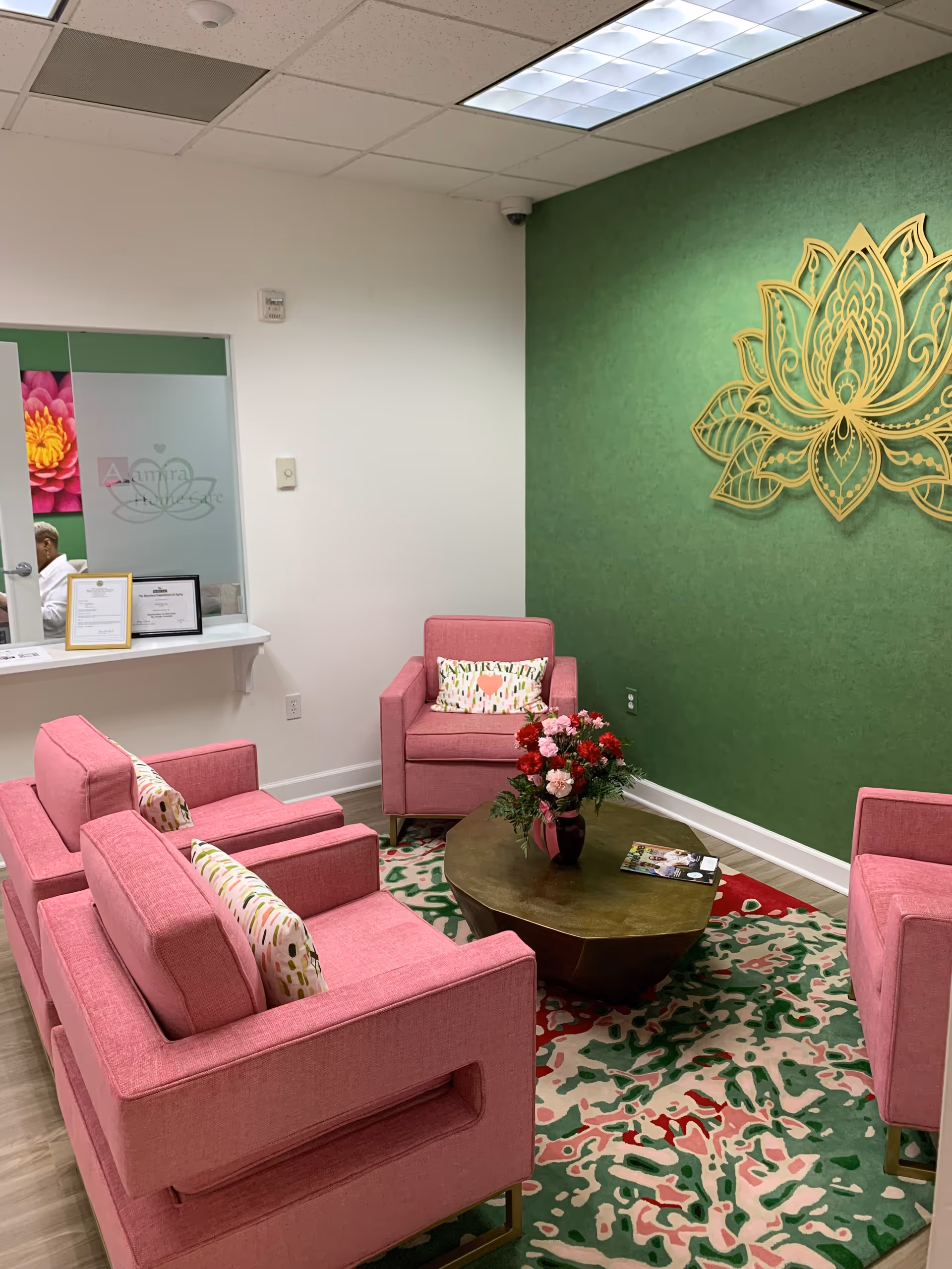 Aamira Home Care lobby lounge with pink chairs, a wooden coffee table, and a green wall.
