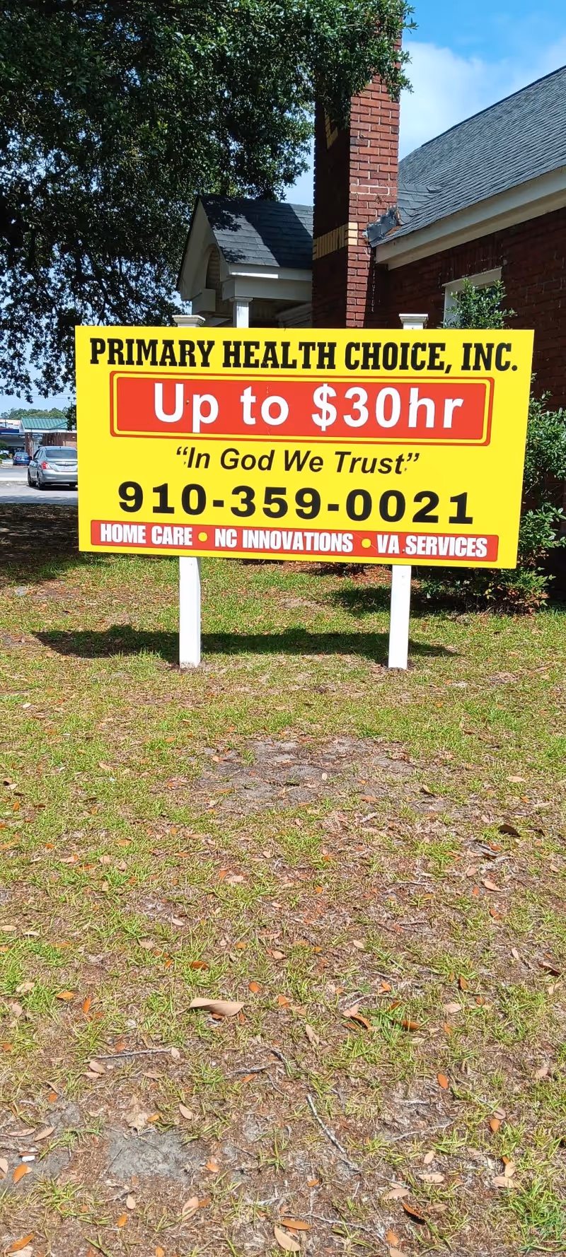 Bright yellow sign for Primary Health Choice on a lawn in front of a brick building