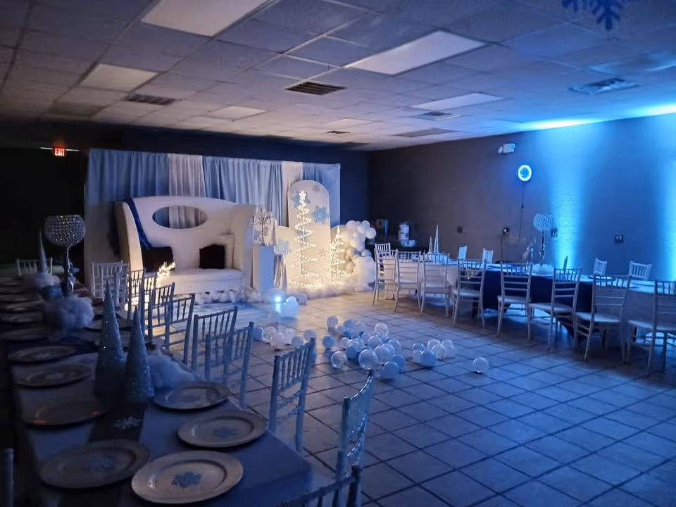 Indoor event hall with blue lighting, white furniture, and winter-themed stage decorations.